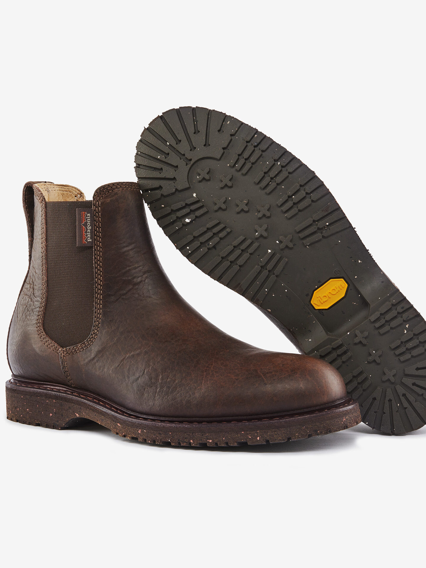 A pair of brown leather Chelsea boots with elastic side panels and rugged rubber soles, shown from a side and sole view.