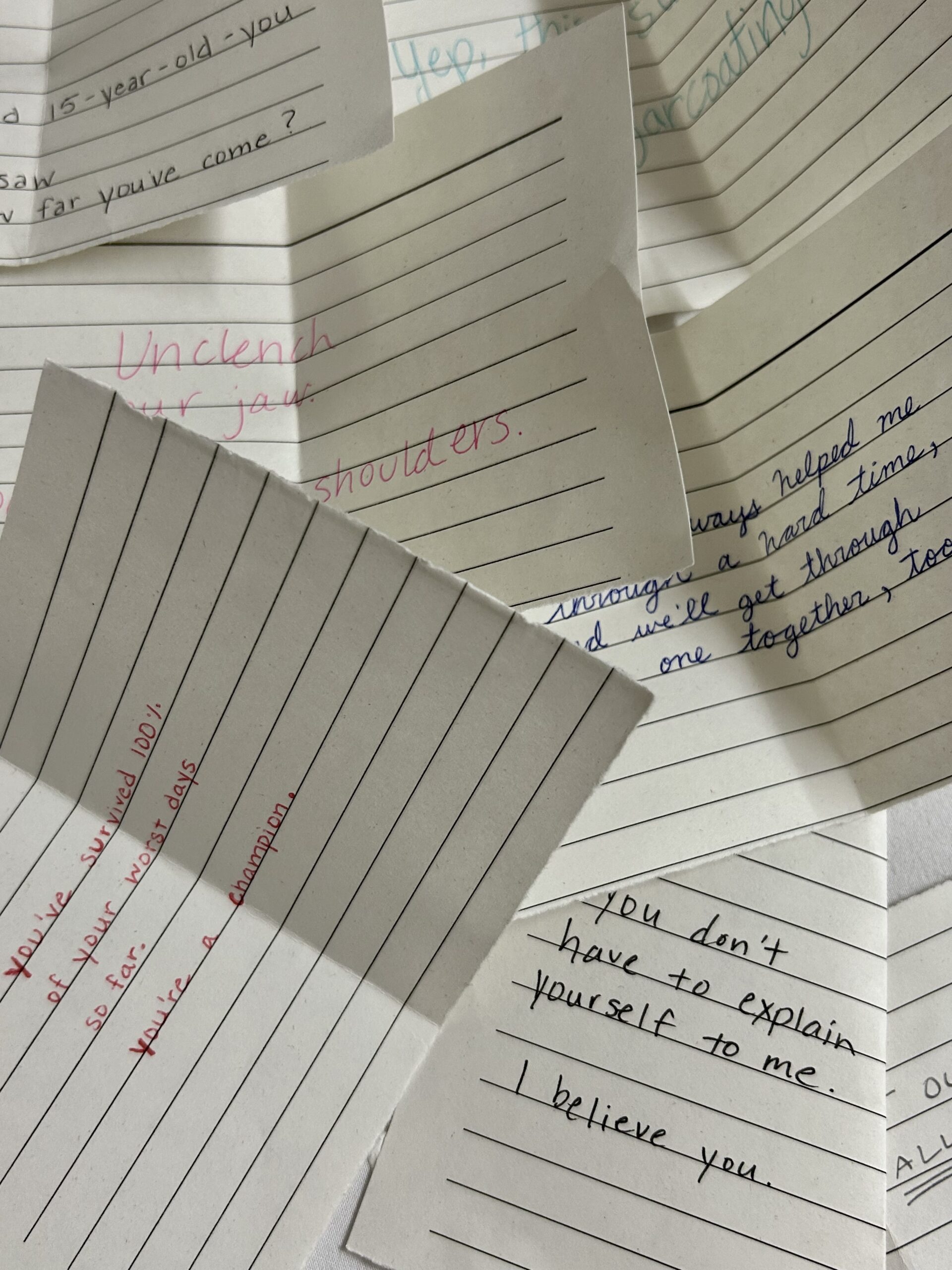 A scattered pile of handwritten notes on lined paper, each containing motivational or supportive messages in various ink colors.