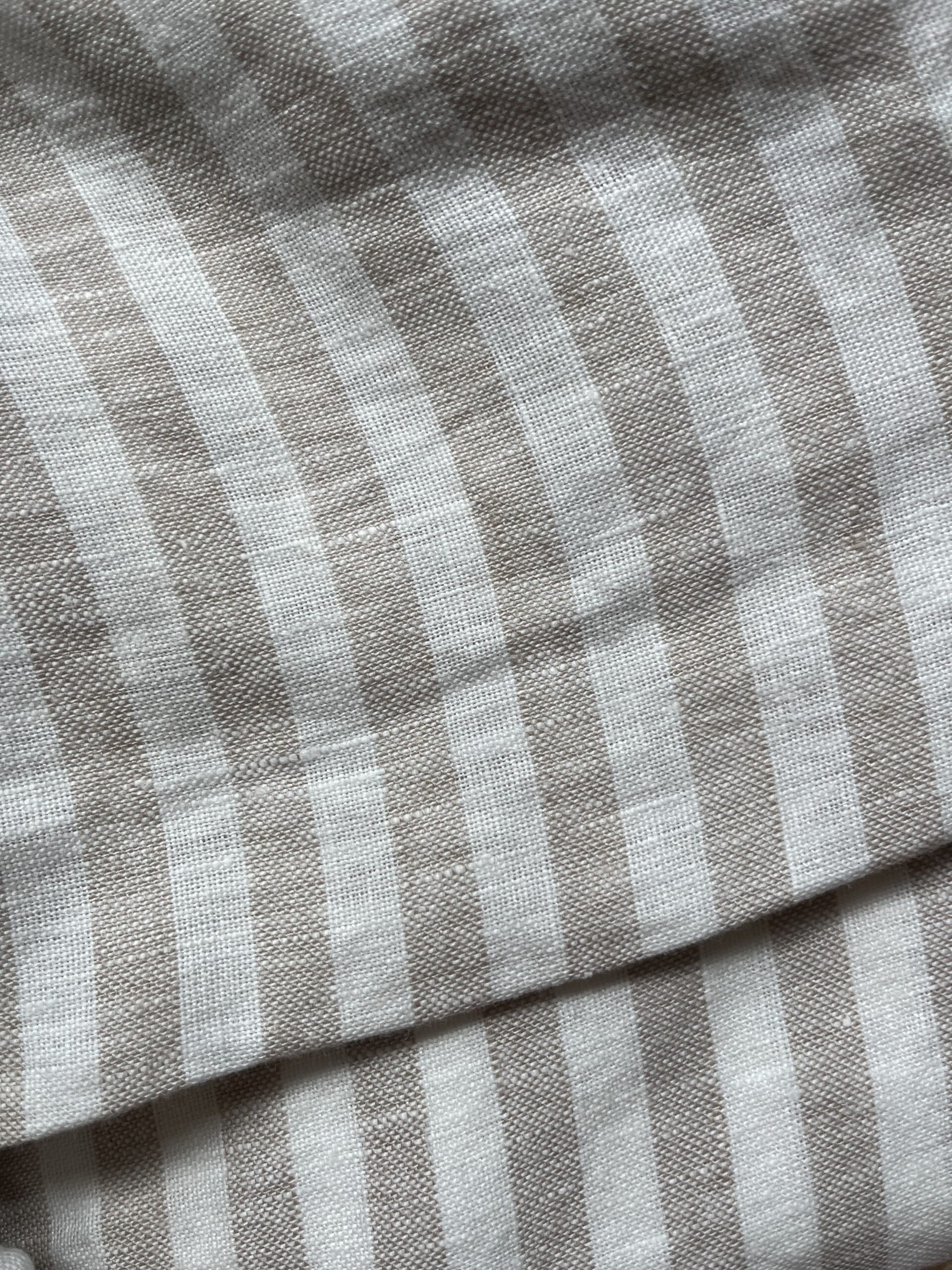 Close-up of a beige and white striped fabric with a soft texture, showing the folds and weave pattern.