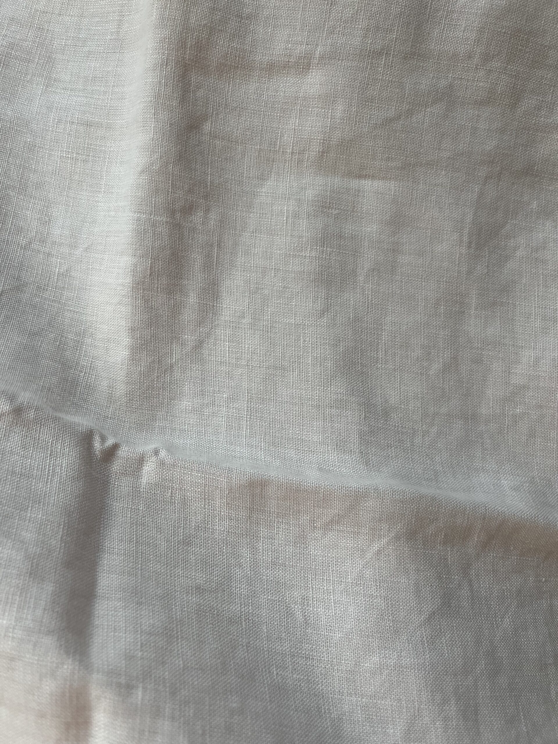 Plain white linen fabric with visible folds and creases. The texture is slightly rough and the material appears lightweight.