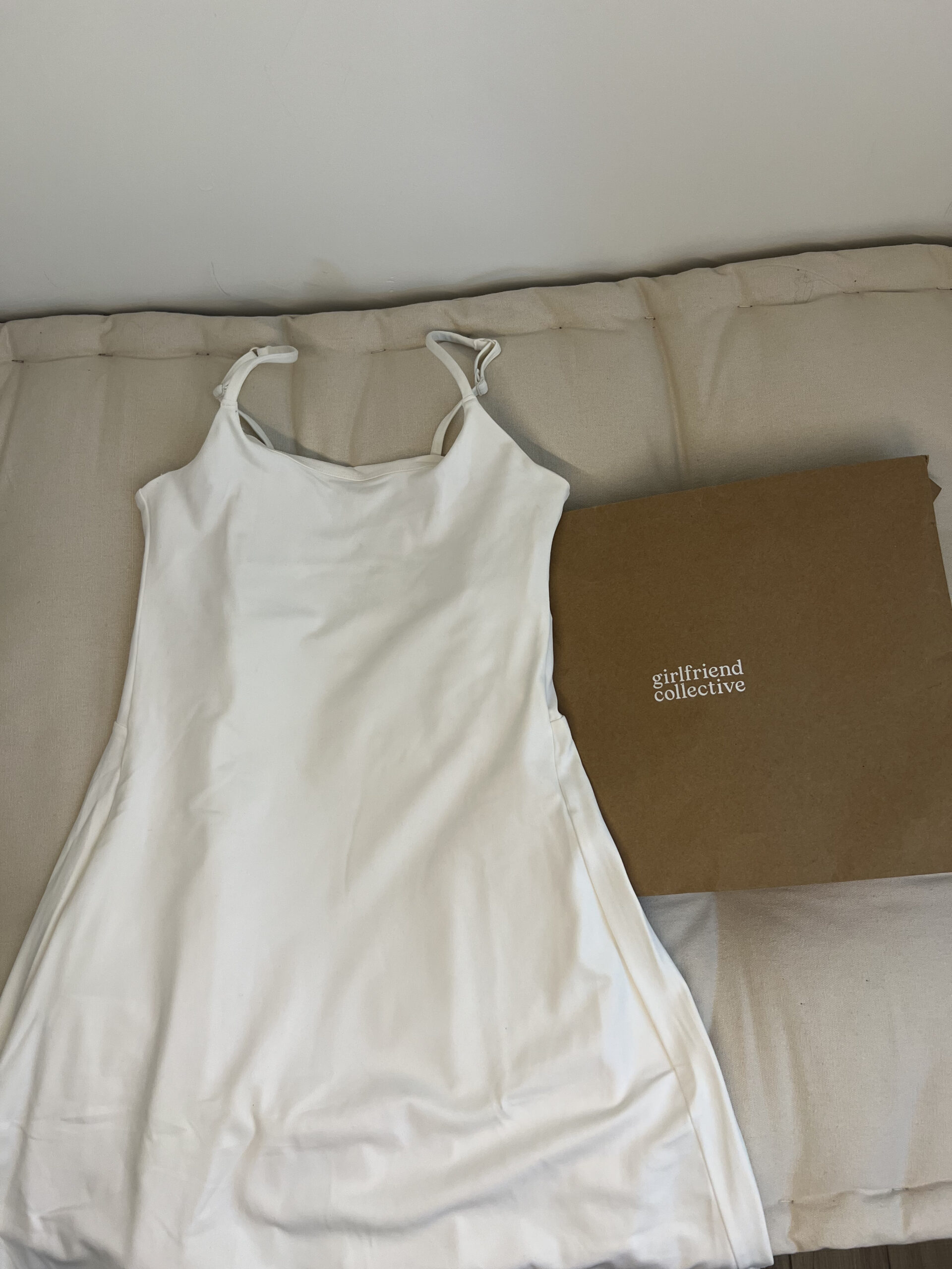 A white dress is laid out on a beige surface next to a brown cardboard box with the text "girlfriend collective" on it.