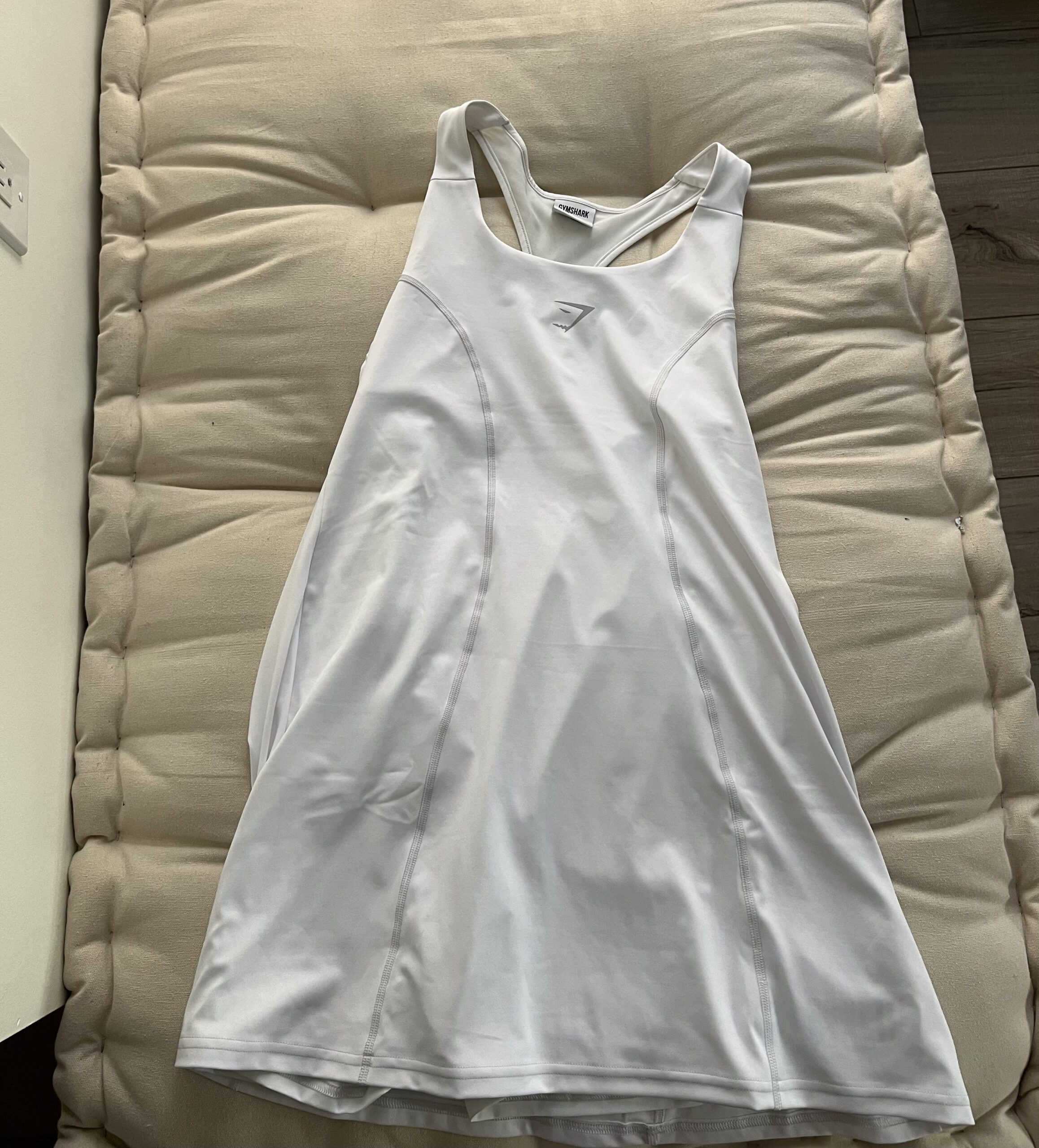 A white sleeveless athletic dress with a simple design lies flat on a cushioned surface.