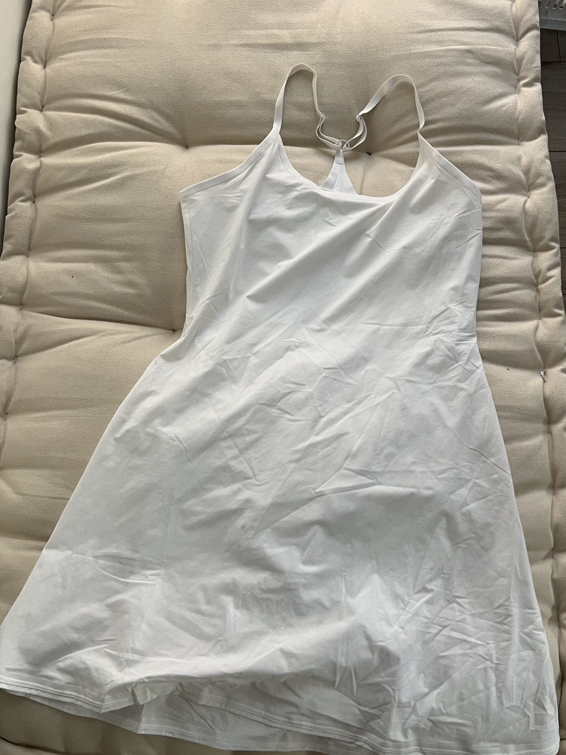 A white sleeveless dress lies flat on a padded beige surface.