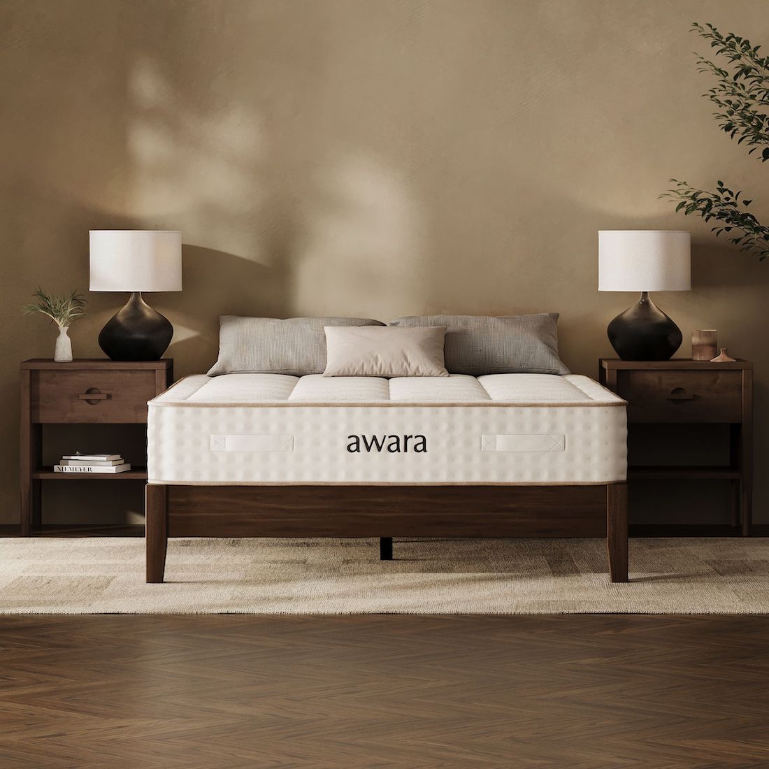 A neatly made bed with "awara" written on the organic mattress, flanked by two wooden nightstands with lamps and decorative items, in a warmly lit bedroom.