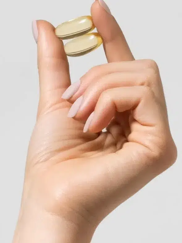 Hand holding two gel capsules with text indicating 1,500mg of EPA and DHA in 2 gelcaps on a light gray background.