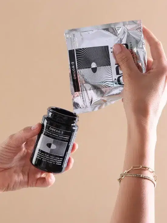 Hands holding a black jar labeled "energy" and a silver sachet, demonstrating the action of pouring contents from the sachet into the jar.