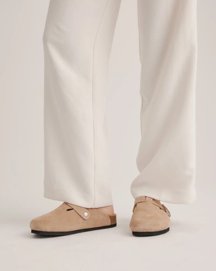 Person wearing white pants and beige slip-on clogs with a single button detail on the side.