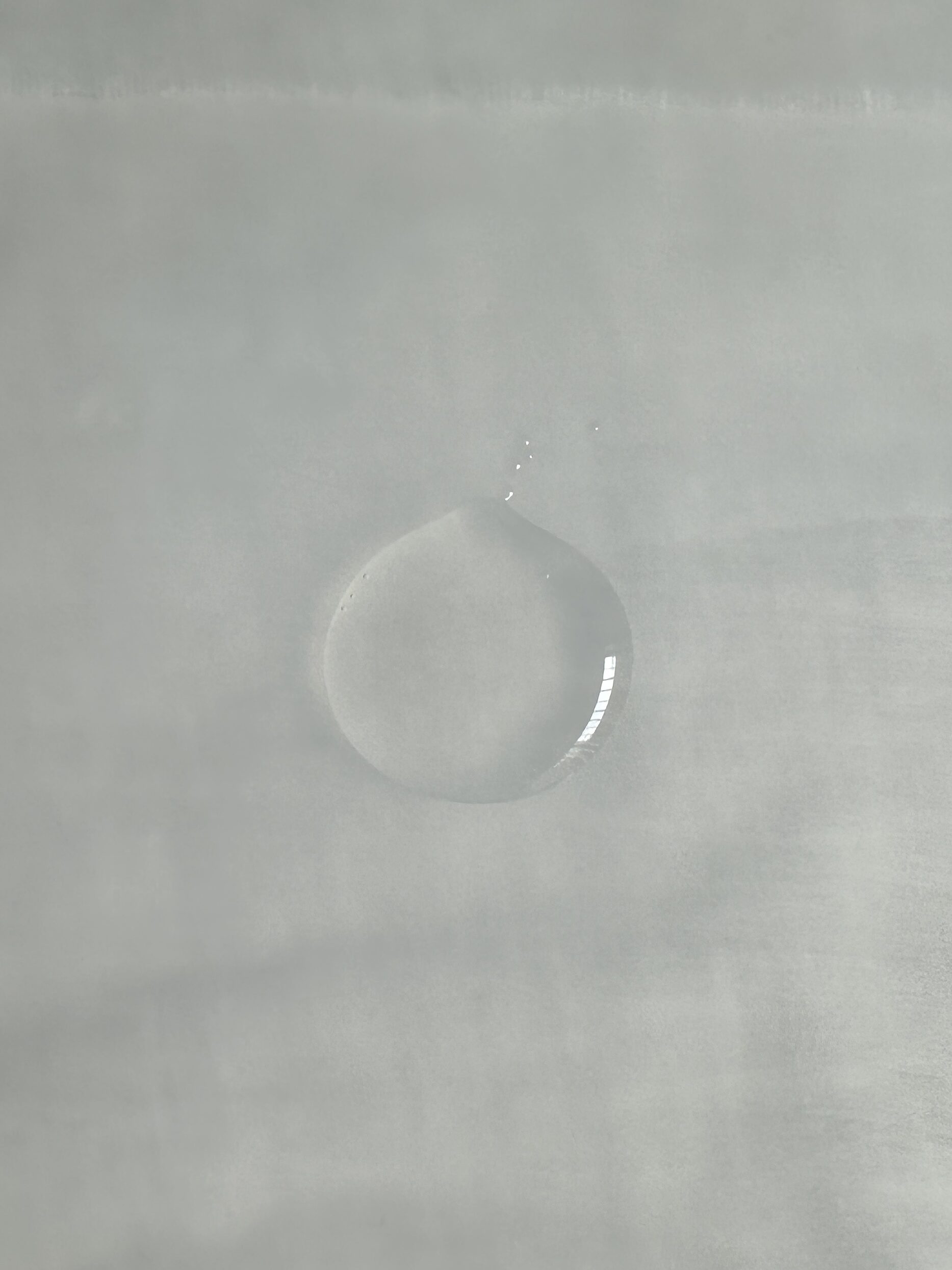 A single droplet of water sitting on a smooth, gray surface.