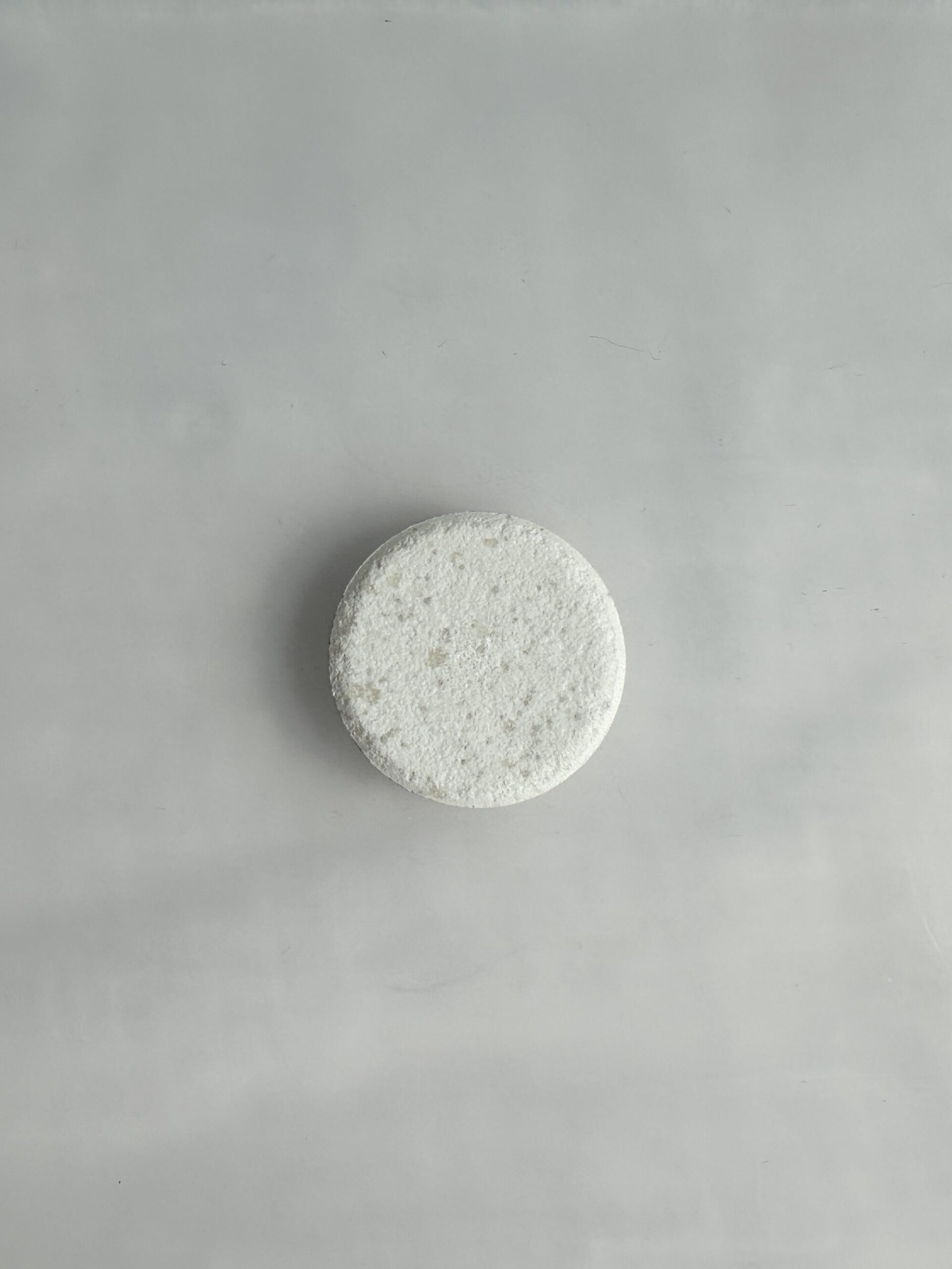 A round white tablet sits on a smooth, light gray surface.