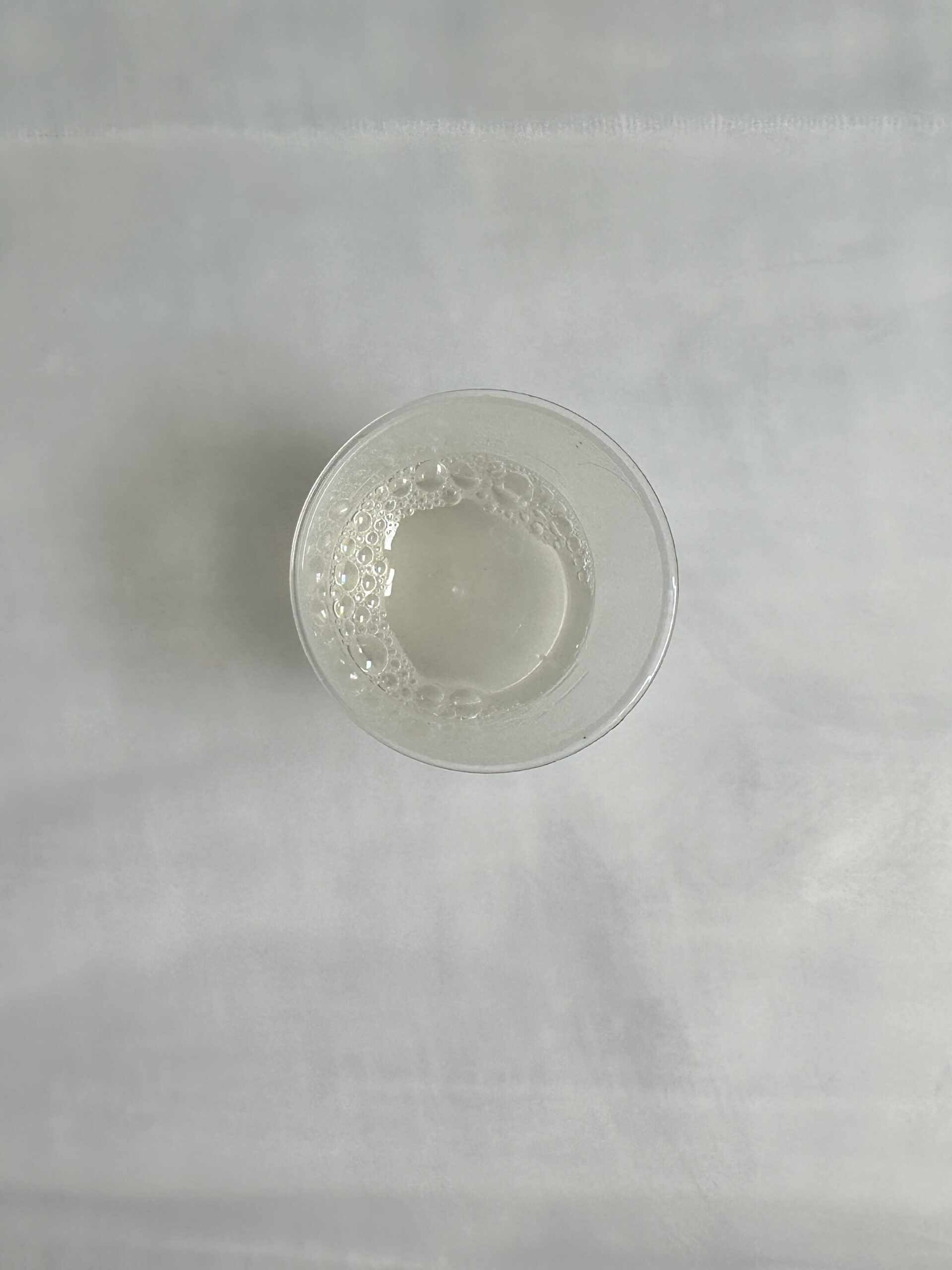 A clear glass of water with bubbles on a light-colored surface.