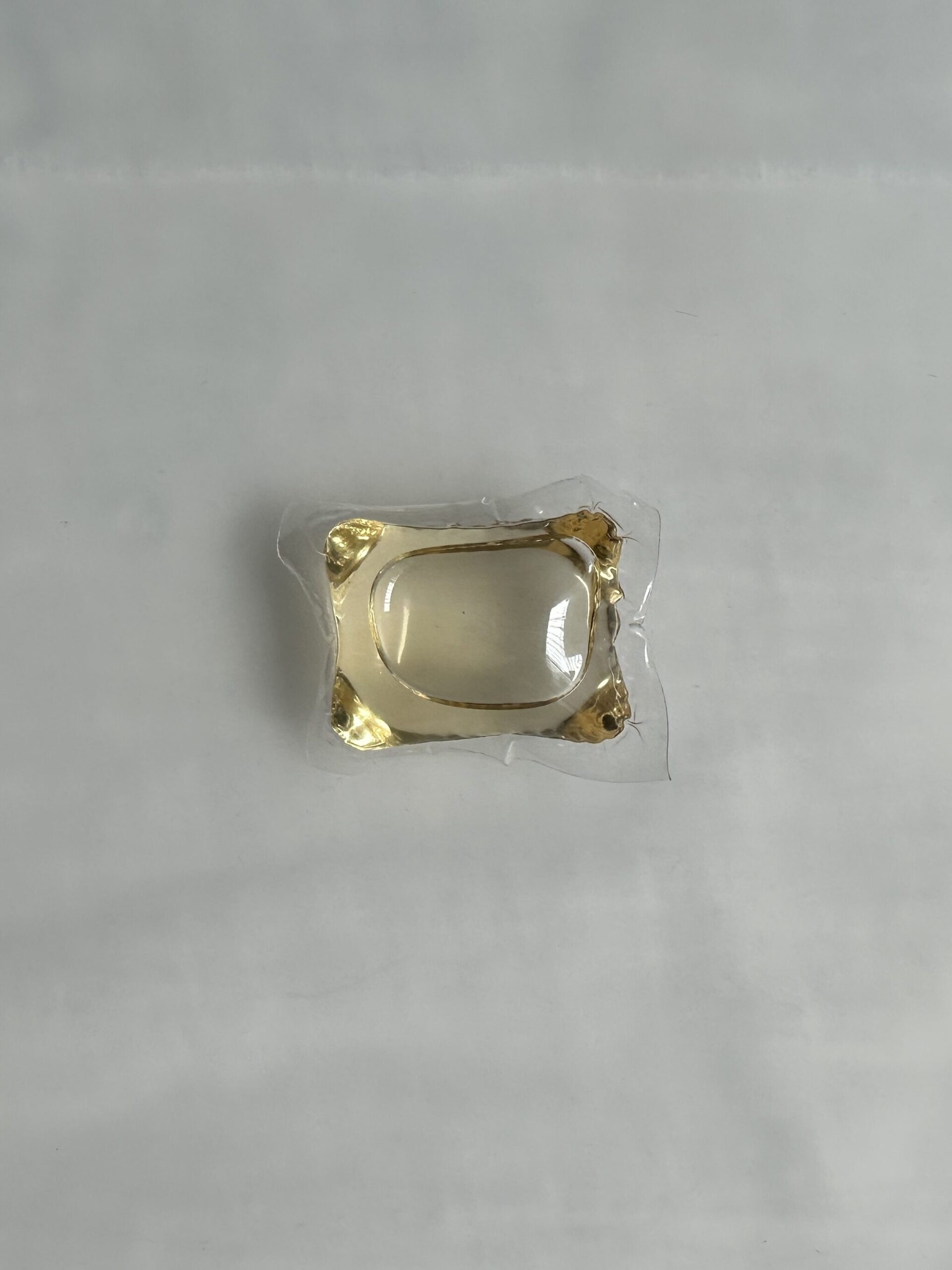 A small rectangular transparent plastic pouch filled with a golden liquid, sealed on all sides and placed against a plain light gray background.