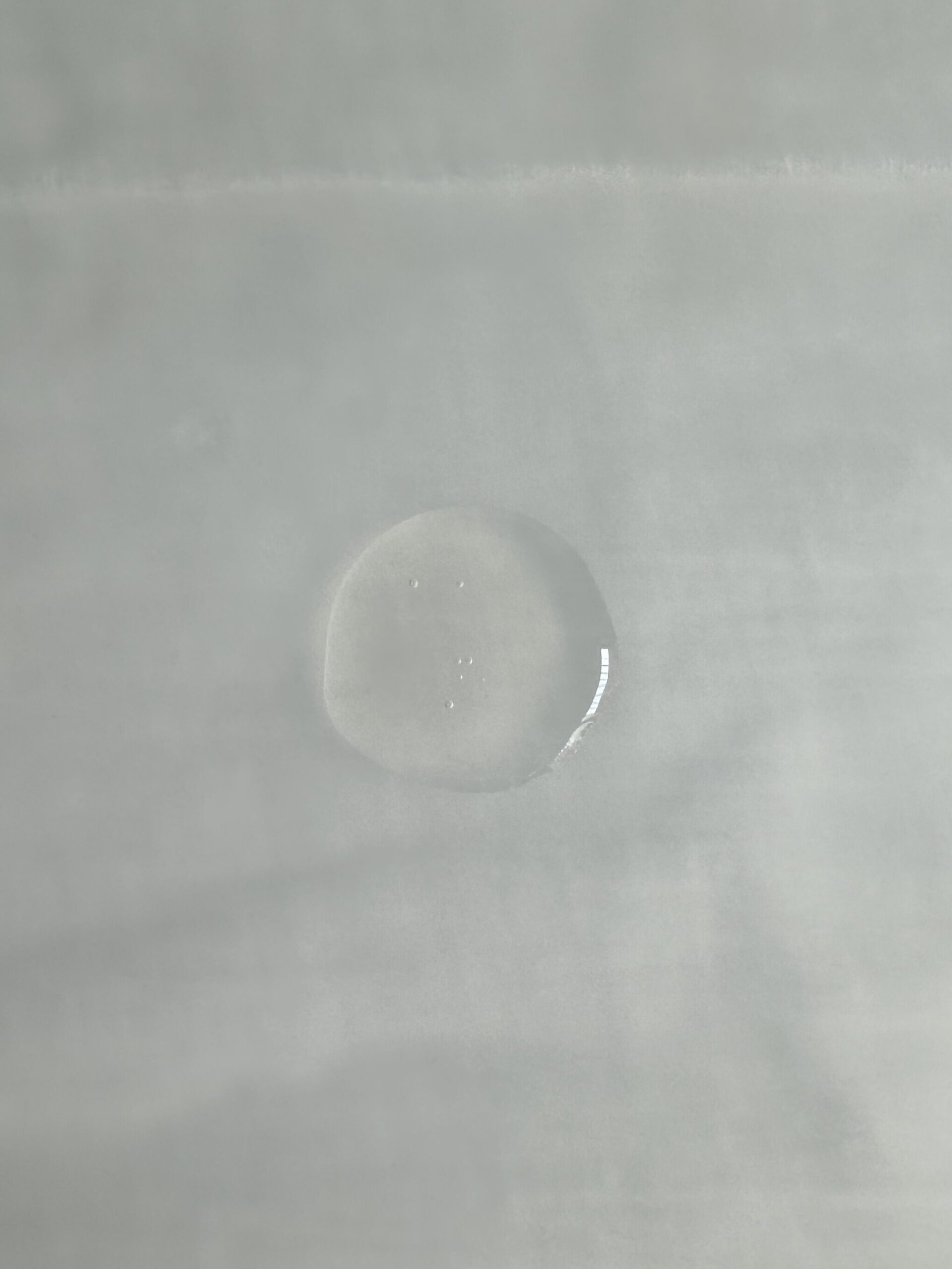 Close-up of a single water droplet on a smooth, light-colored surface.