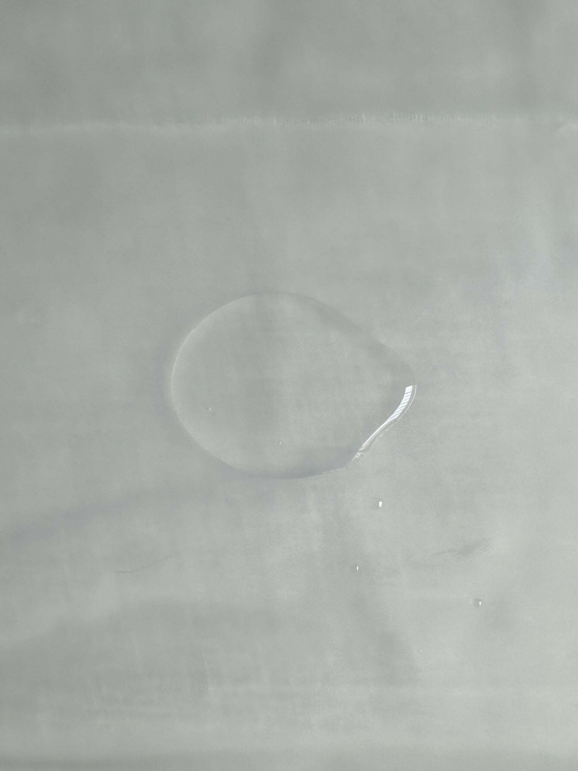 A single drop of clear liquid on a smooth, light-colored surface.