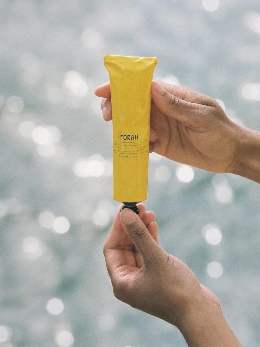 Person holding a yellow tube of FORAH Recovery Hand Cream against a blurred outdoor background.