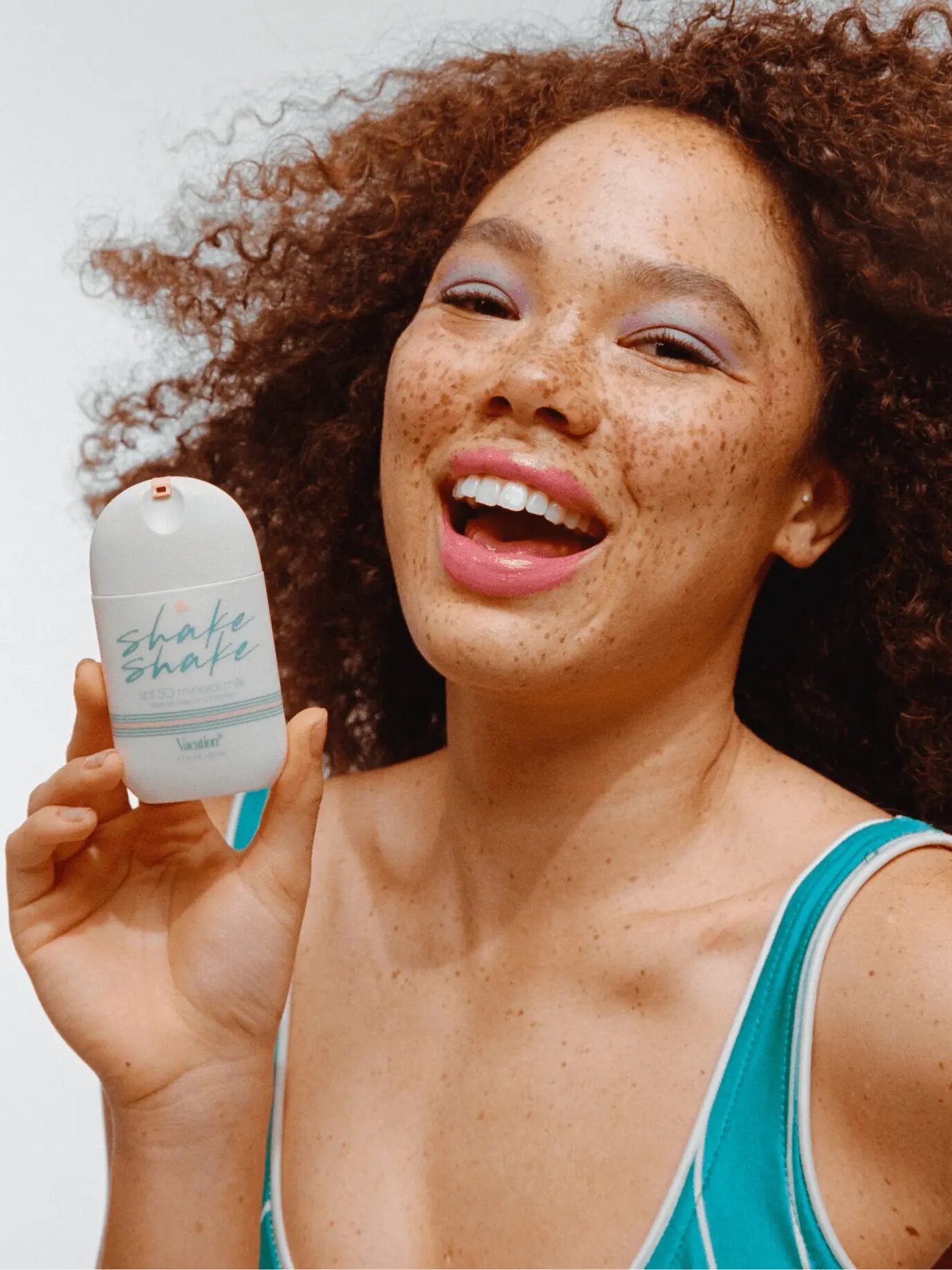 Person with curly hair and freckles smiling and holding a container labeled "Shake Shake.