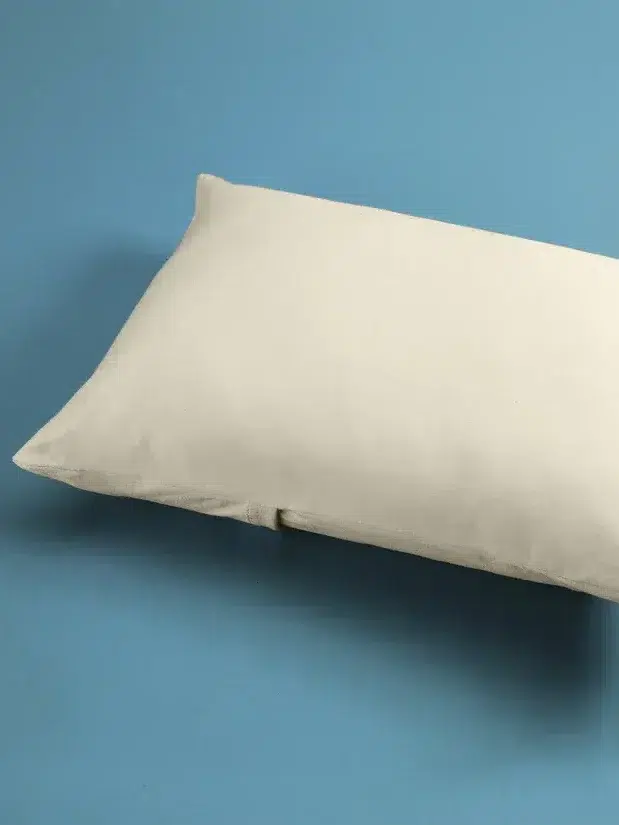 A plain white rectangular pillow is placed on a light blue surface.