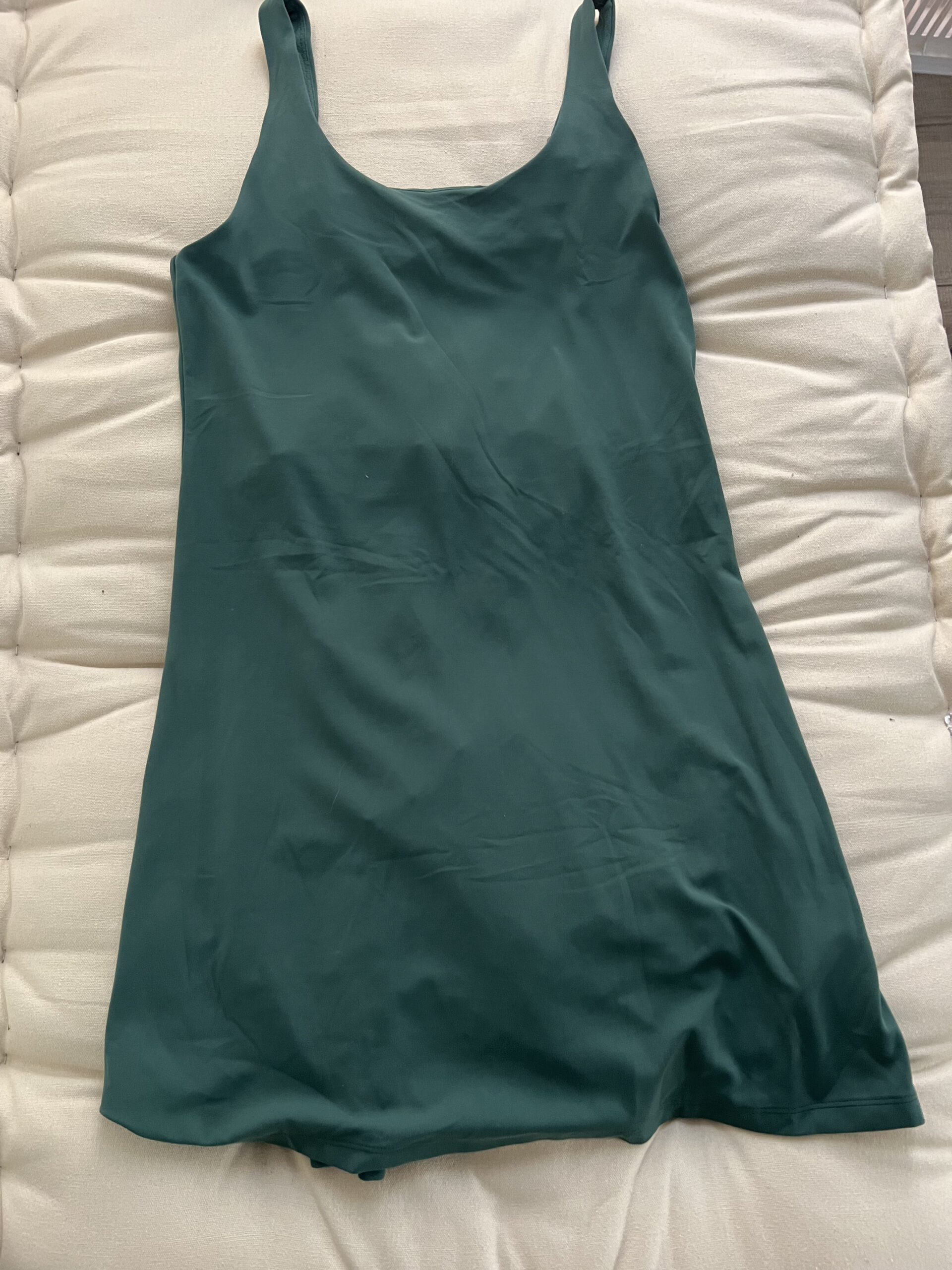 A green sleeveless dress with a scoop neckline is laid flat on a textured off-white surface.