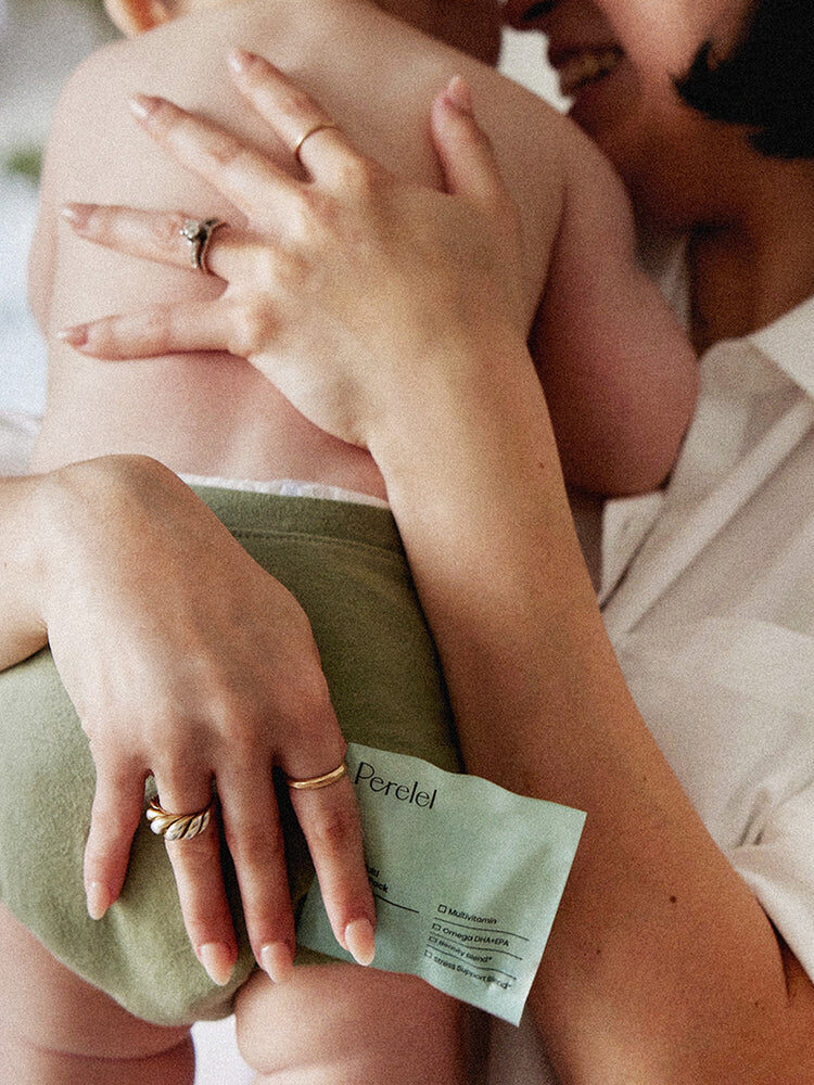 A person wearing a white shirt holds a baby dressed in a green diaper. The person holds a product package labeled "Perel" in their left hand.