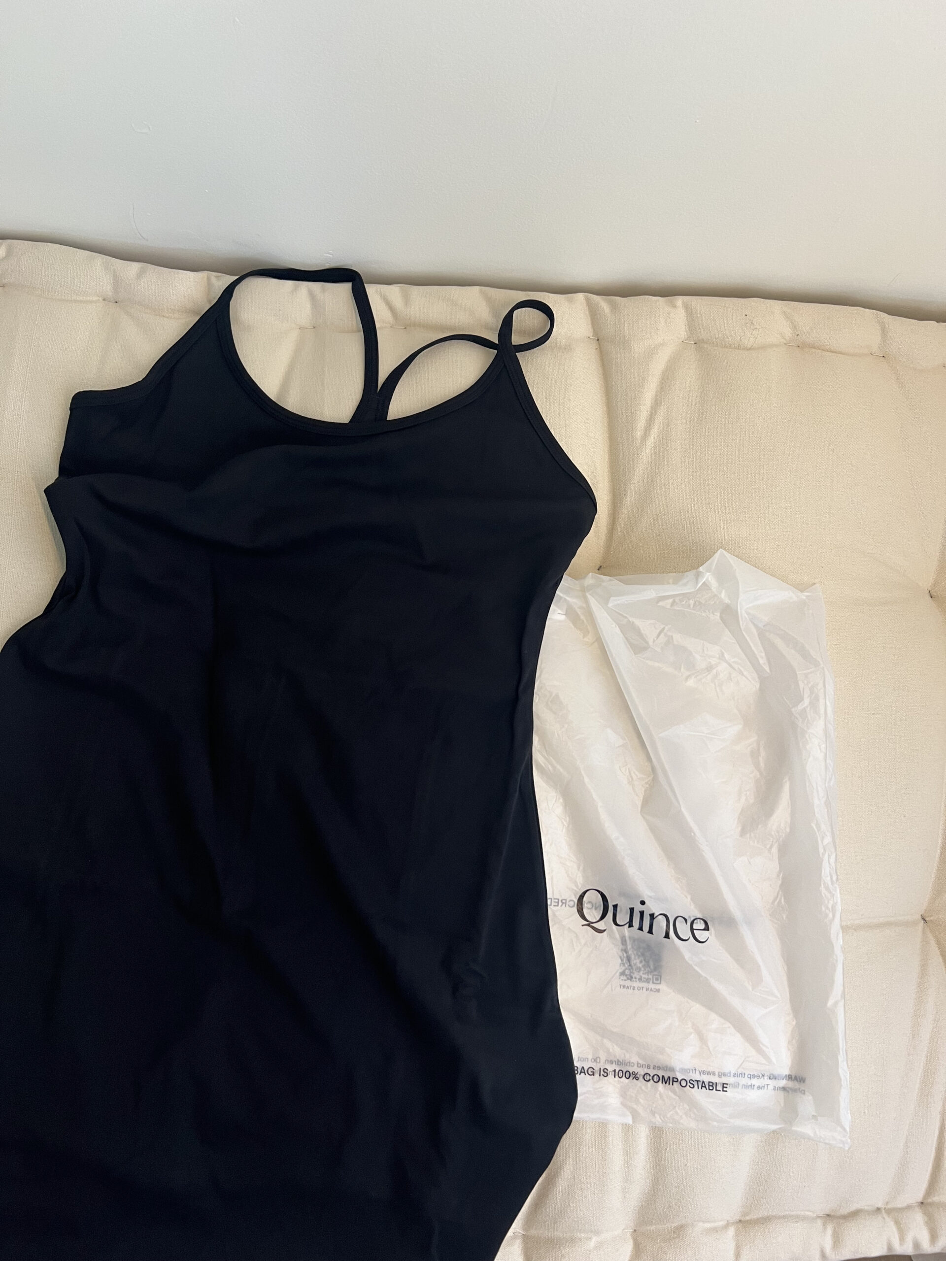 A black tank top lies on a cushioned surface beside a white plastic bag labeled "Quince.