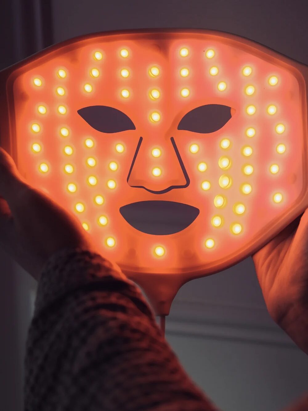 Person holding an LED face mask with orange lights illuminated.