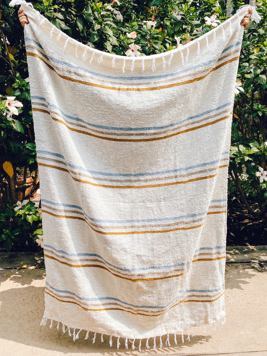 Person holding up a white towel with yellow and blue stripes in front of a flowering shrub.