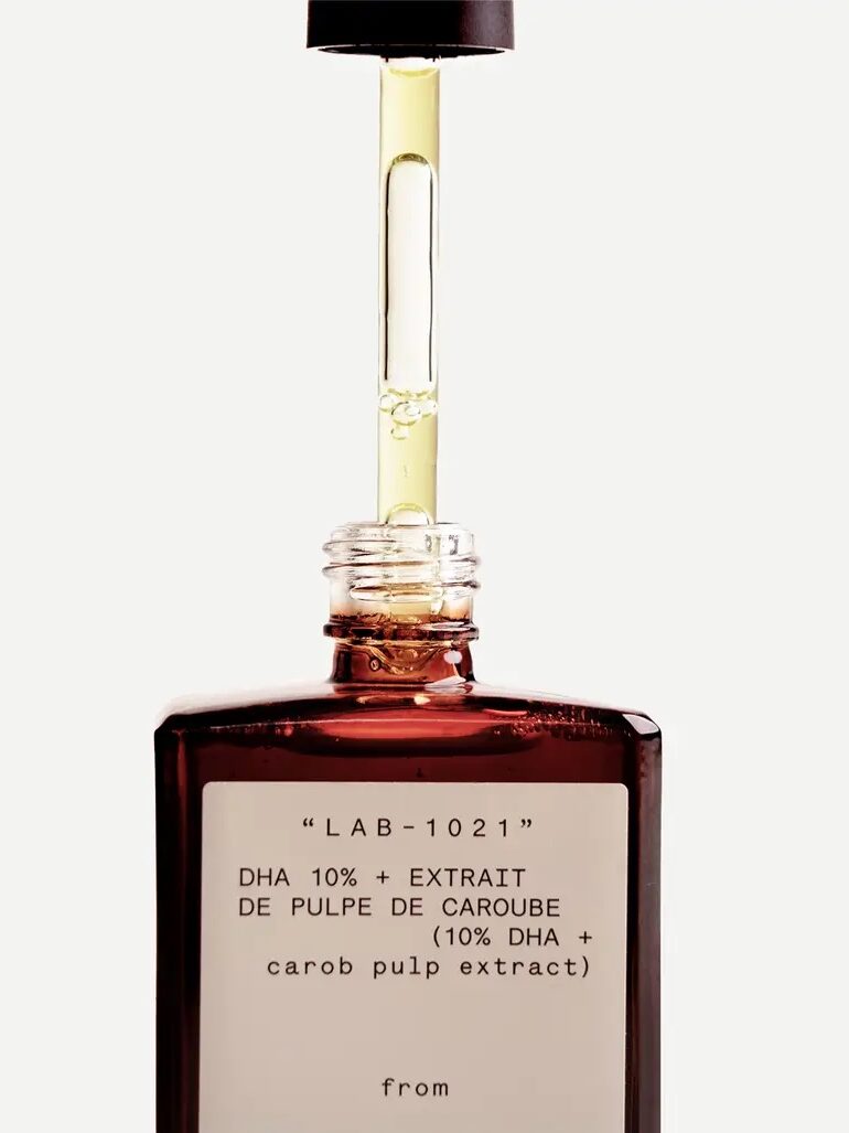 A dropper with yellow liquid suspended above an amber glass bottle labeled "LAB-1021" containing DHA 10% and carob pulp extract.