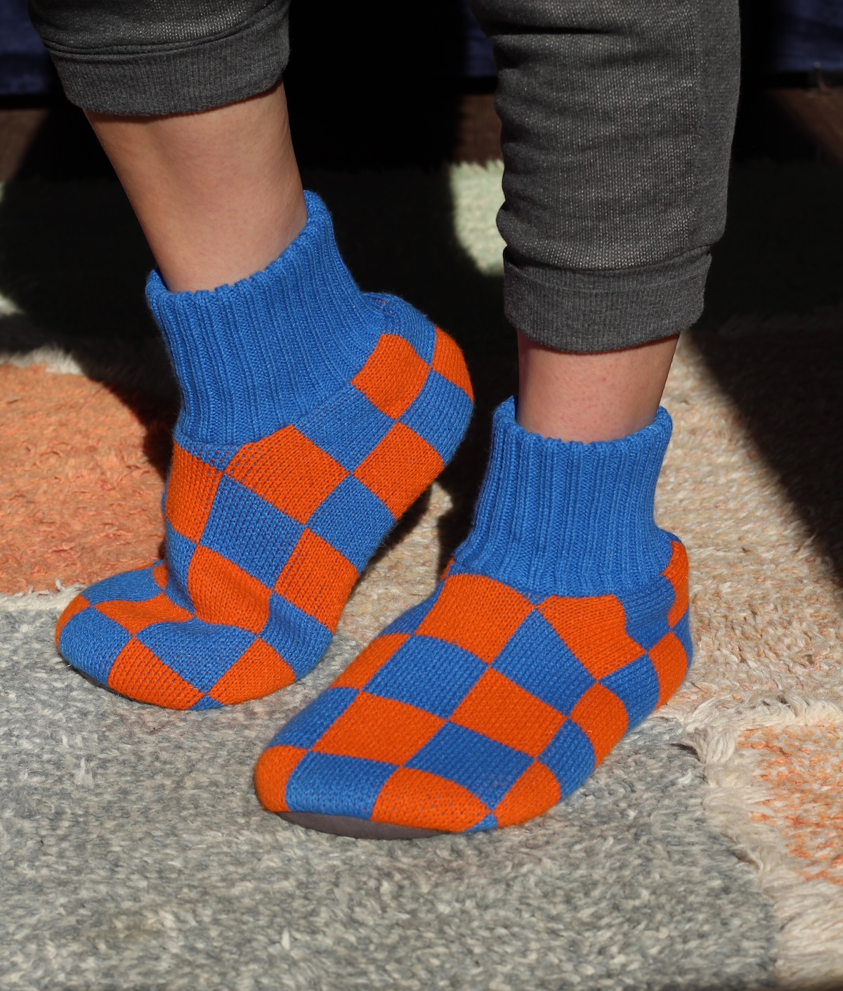 Person wearing blue and orange checkered socks and gray pants on a multicolored rug.