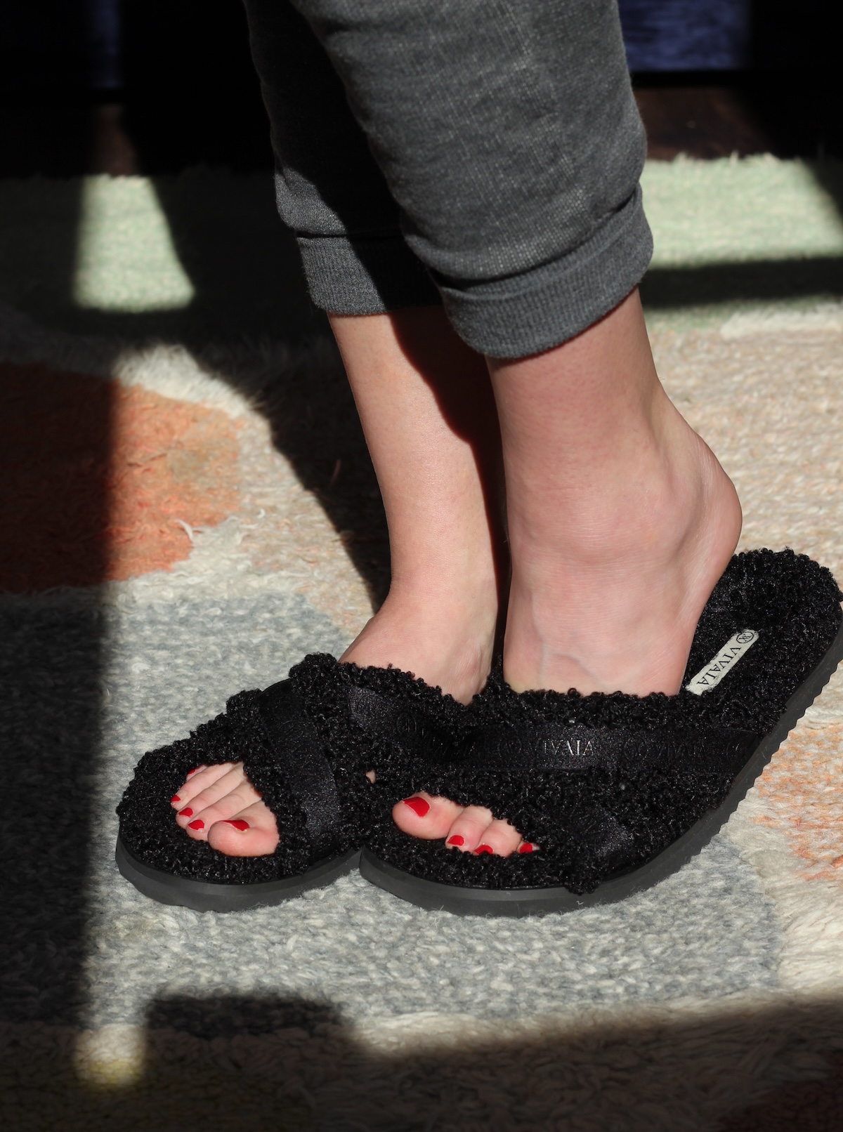 A person wearing black fuzzy slippers stands on a colorful rug.