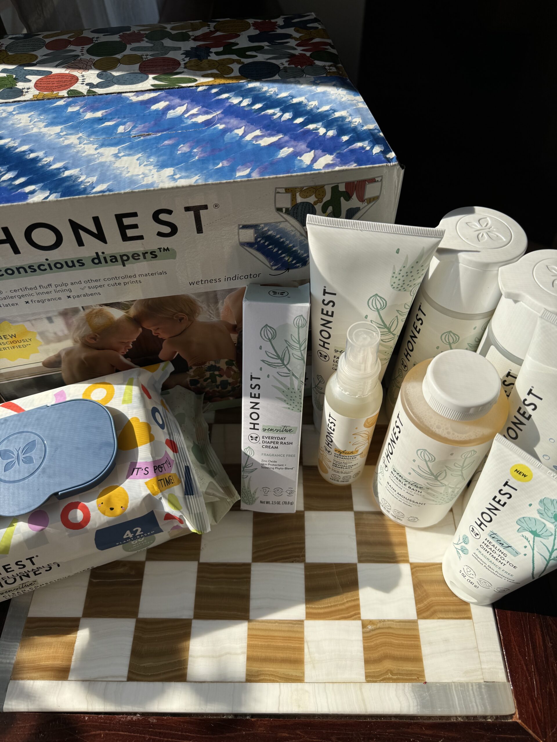 A collection of Honest brand baby care products including diapers, wipes, lotions, and shampoos displayed on a wooden surface.