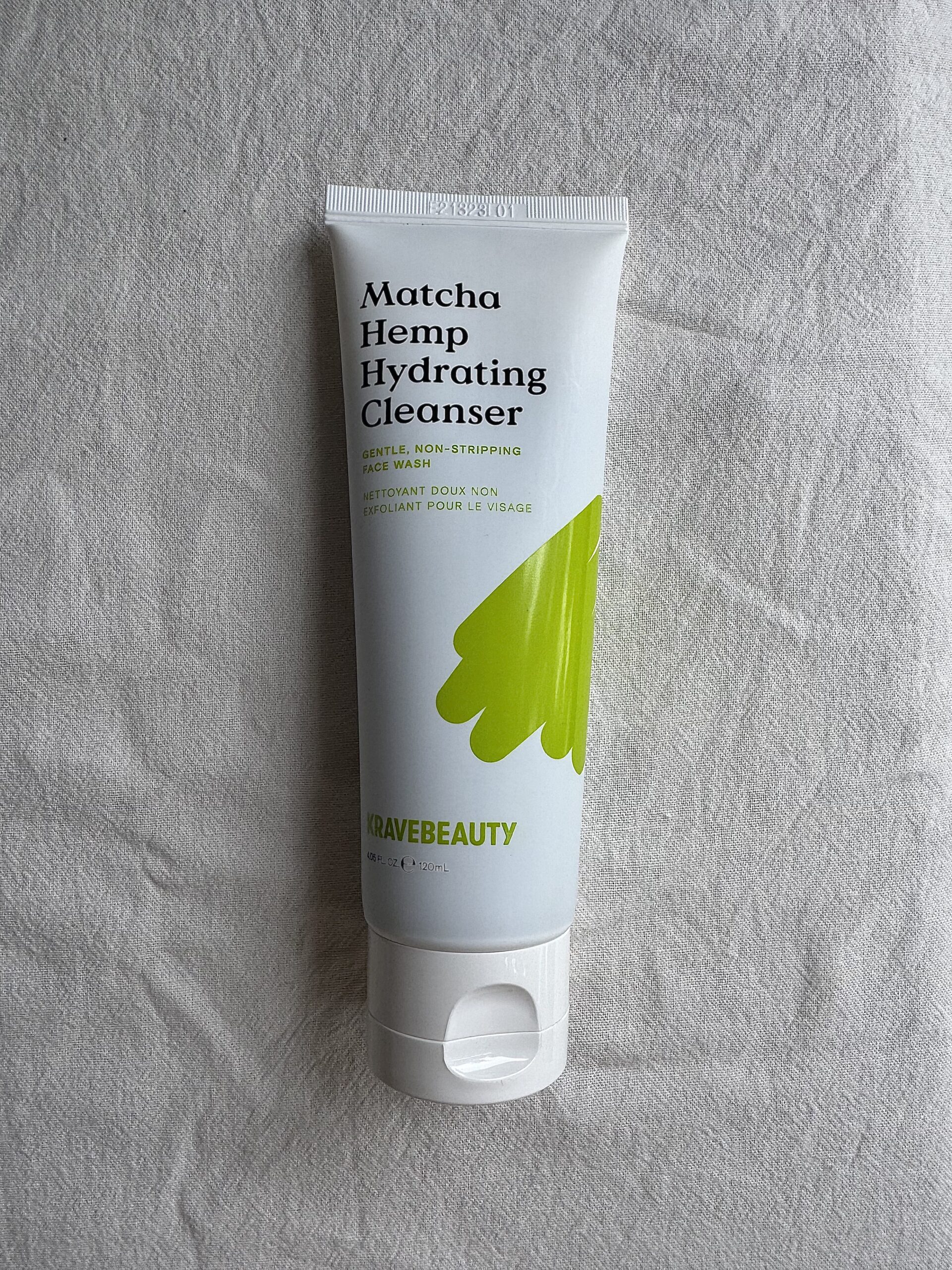 A tube of KRAVEBEAUTY face wash on a white fabric surface. 