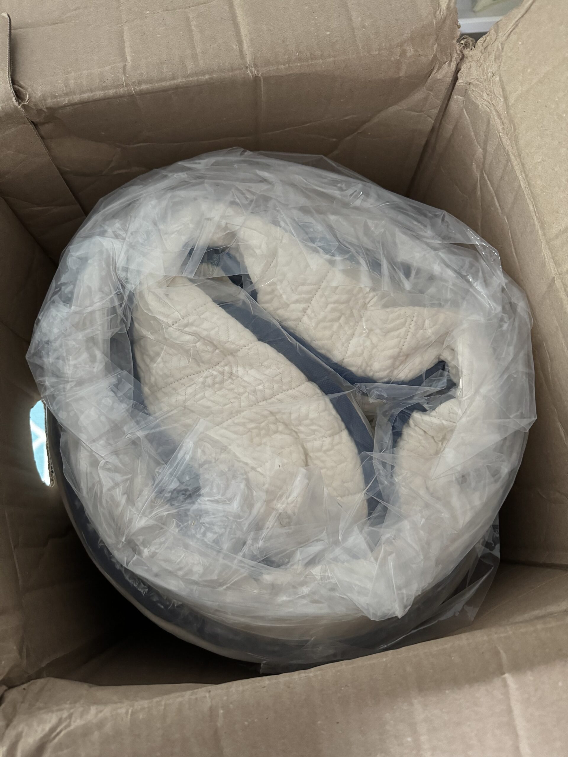 A pair of white sneakers wrapped in plastic inside an open cardboard box.