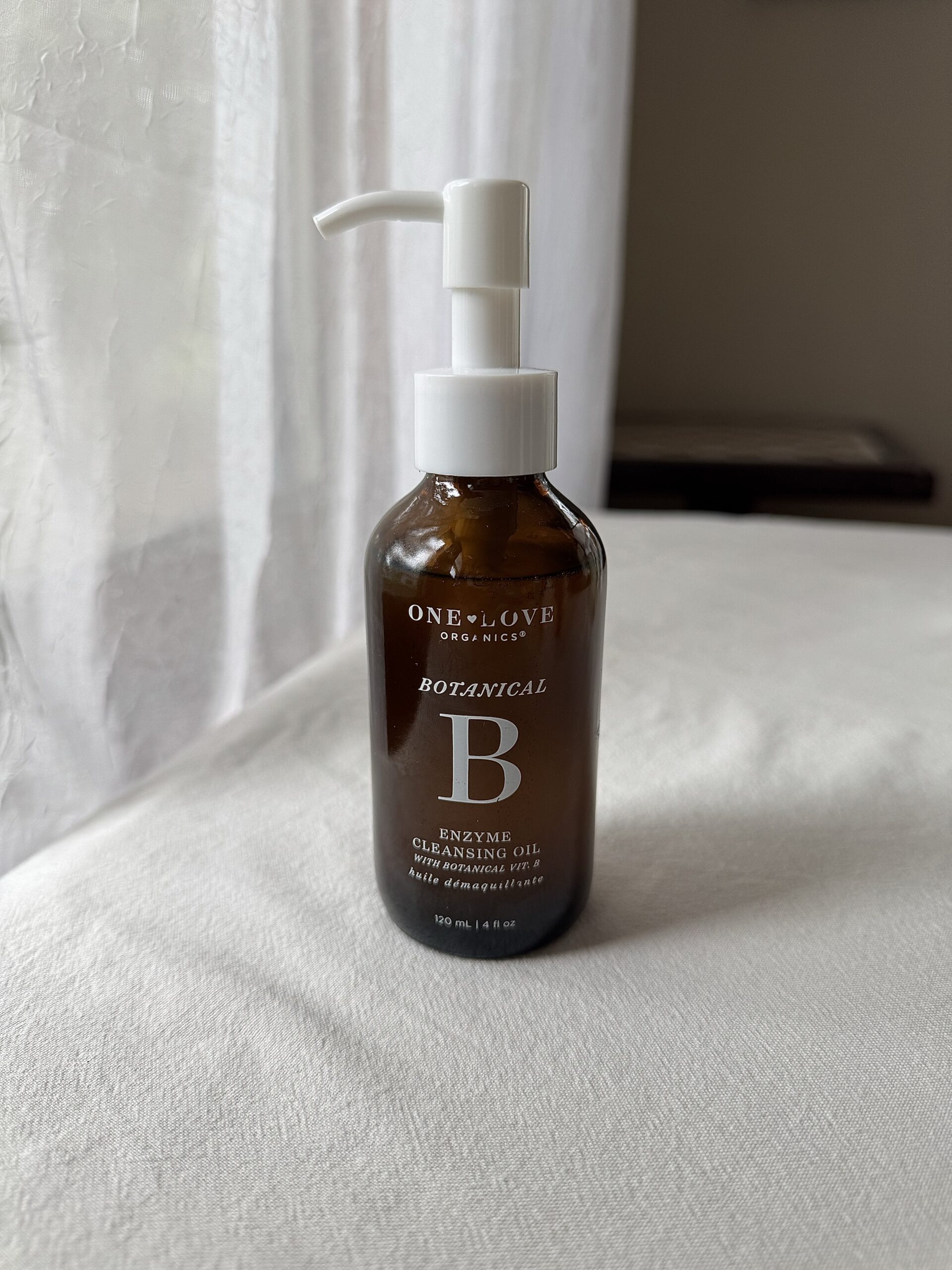 A bottle of One Love Organics face wash sitting on a white fabric surface. 