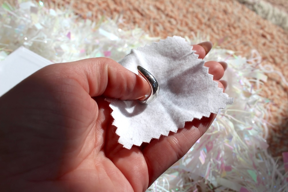 Hand holding a silver ring and a white polishing cloth, with a background of shredded paper.