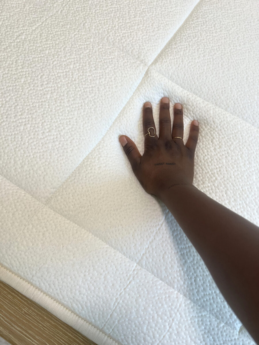 A hand with rings presses down on a white, textured mattress.