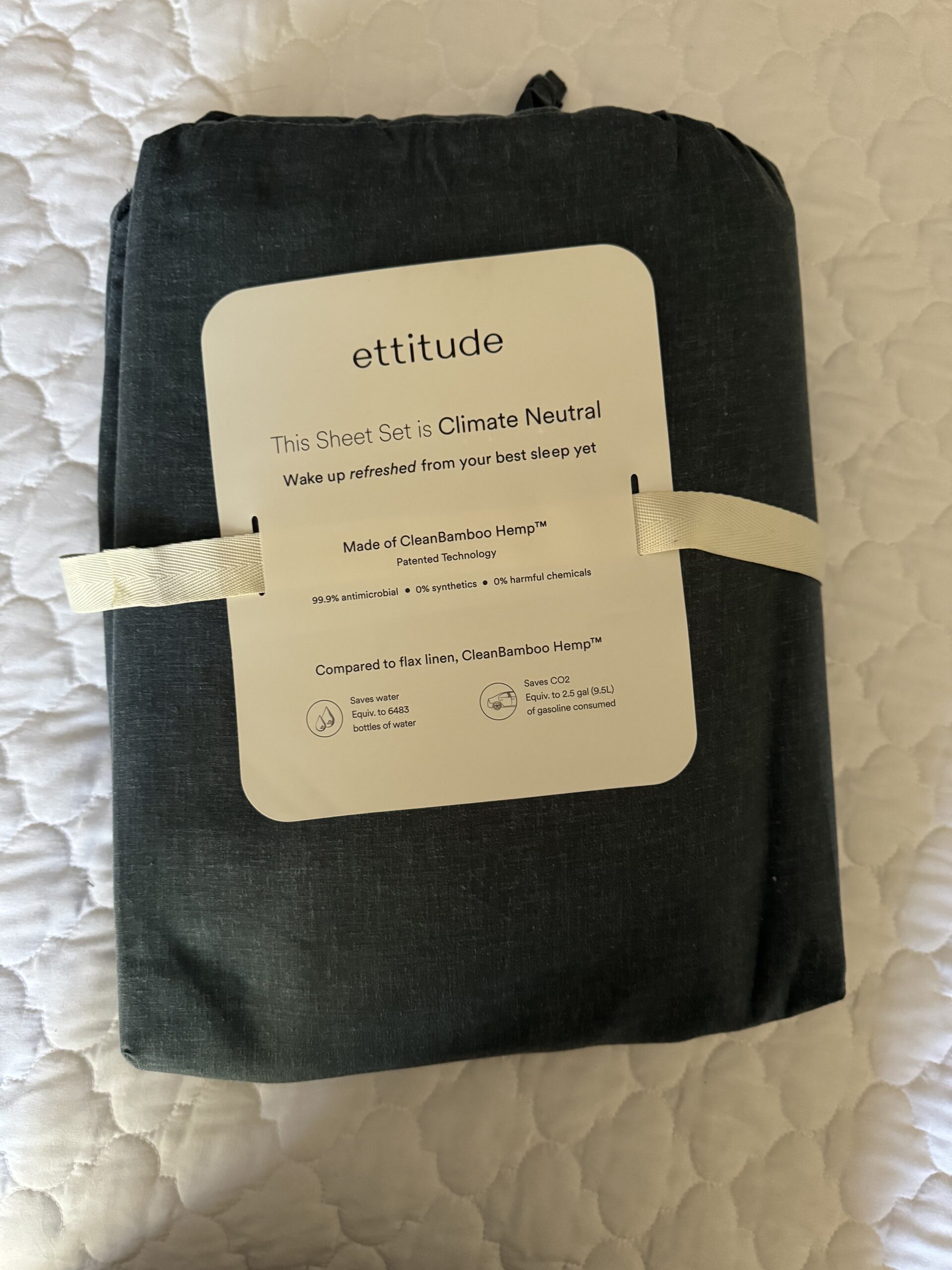 A packaged dark gray sheet set from ettitude, labeled as climate neutral and made of CleanBamboo Hemp, on a white quilted surface.