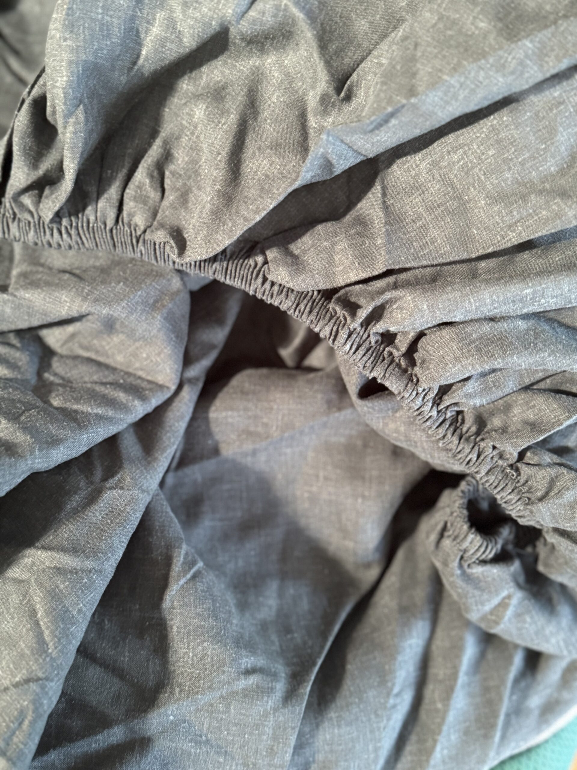 Close-up of a gray, wrinkled, elastic-edged fabric, possibly a fitted bed sheet, with gathered and stretched sections visible.