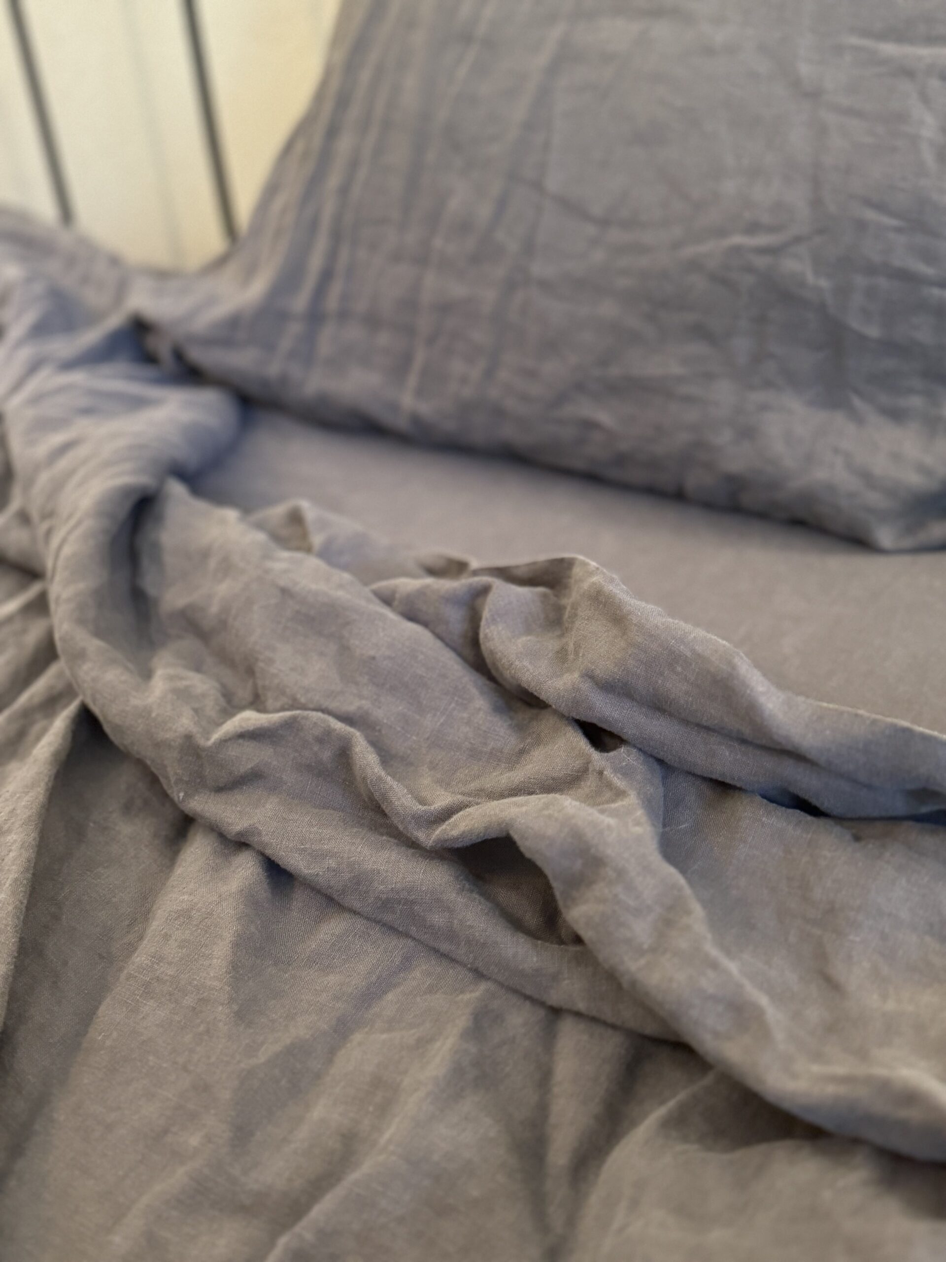 Close-up of a rumpled gray bed sheet and pillowcase on an unmade bed. The fabric appears soft and slightly wrinkled, with a textured surface.
.