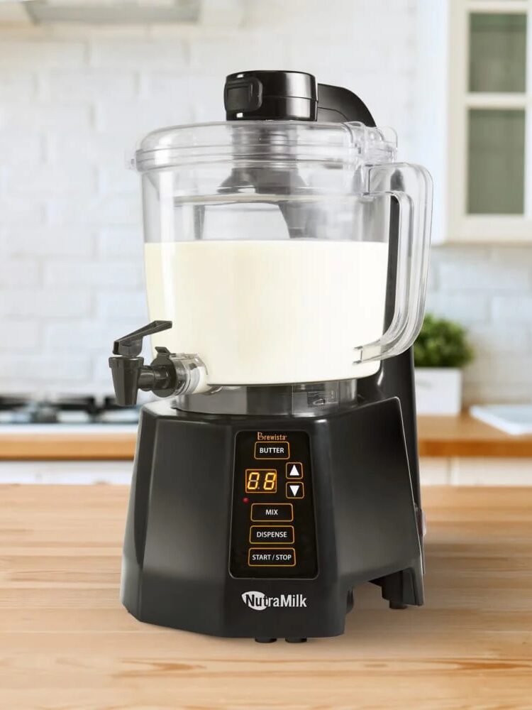 A black kitchen appliance labeled "NutraMilk" is placed on a countertop, with a transparent container filled with milk and various control buttons on the front.