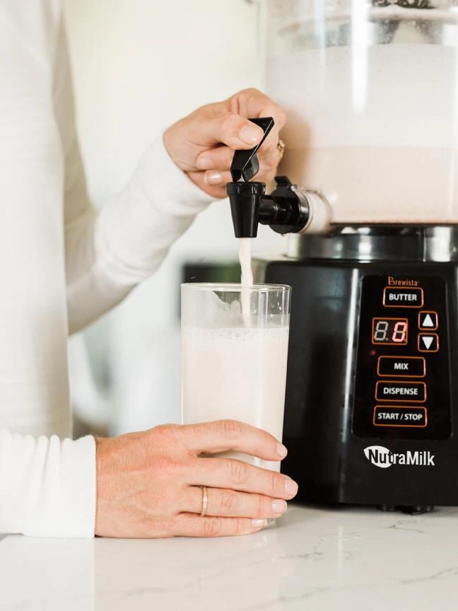 A person dispensing a beverage from a NutraMilk machine into a tall glass.