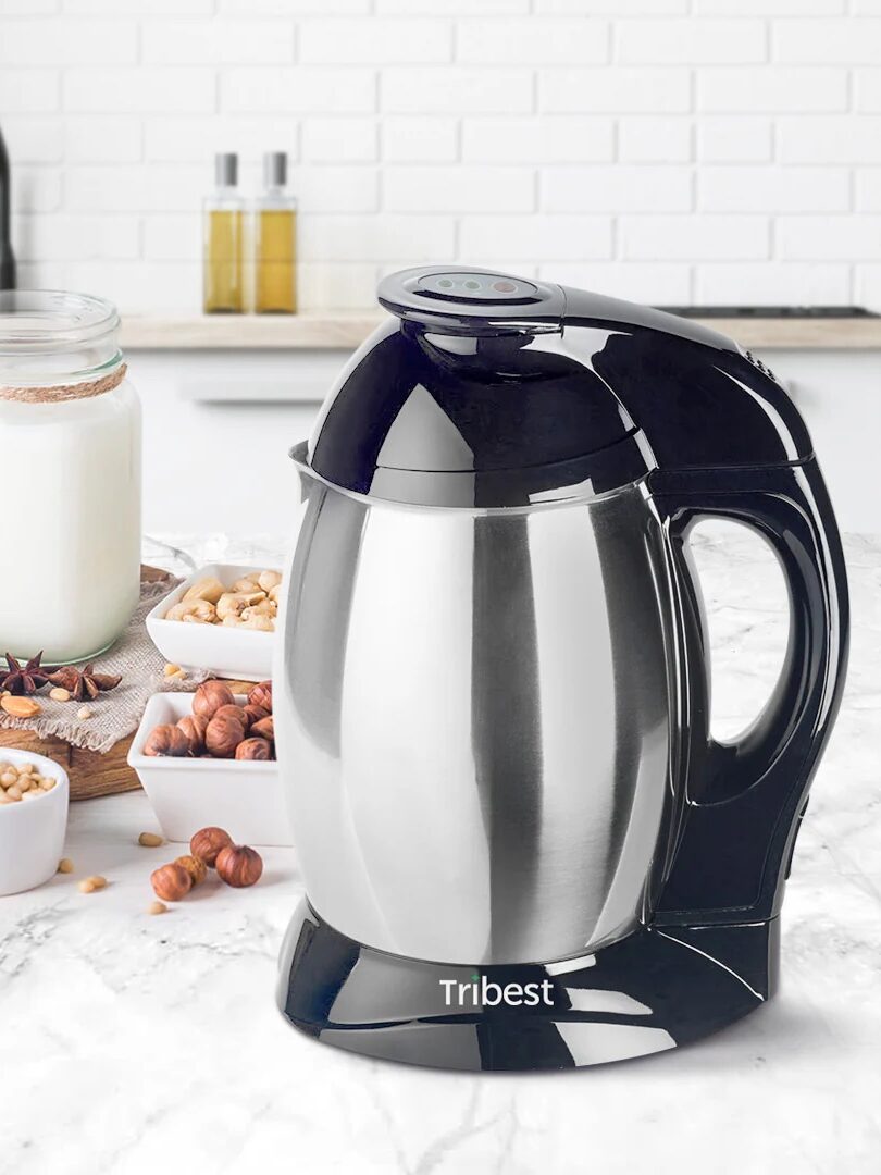 A black and silver Tribest appliance sits on a marble countertop surrounded by various nuts, a jar of milk, and a white kitchen background.