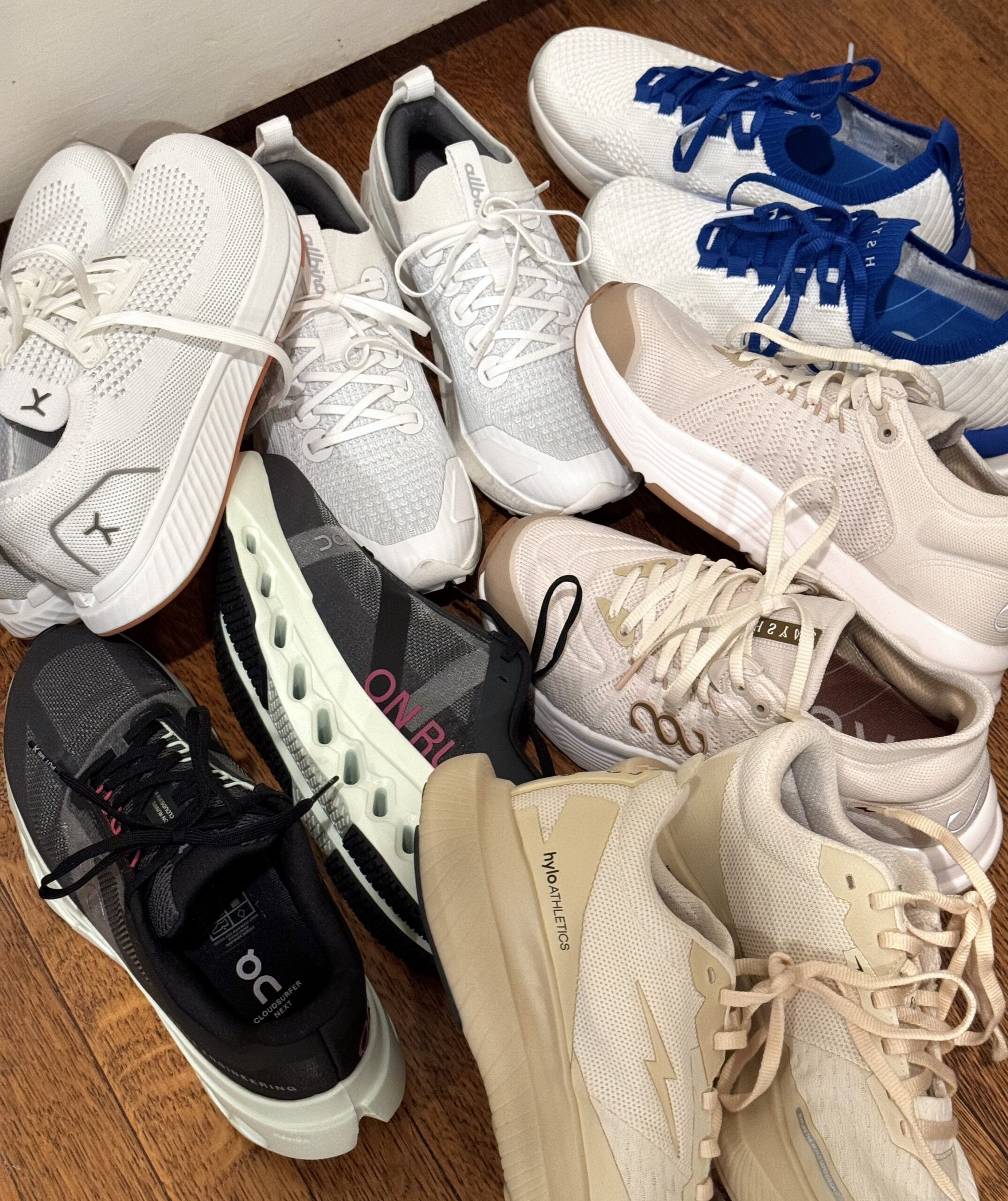 A variety of sneakers in different styles and colors are arranged on a wooden floor.