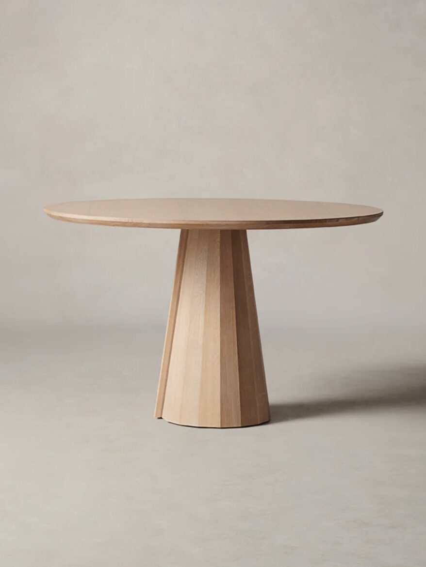 A wooden round table with a tapered, faceted pedestal base on a light grey background.