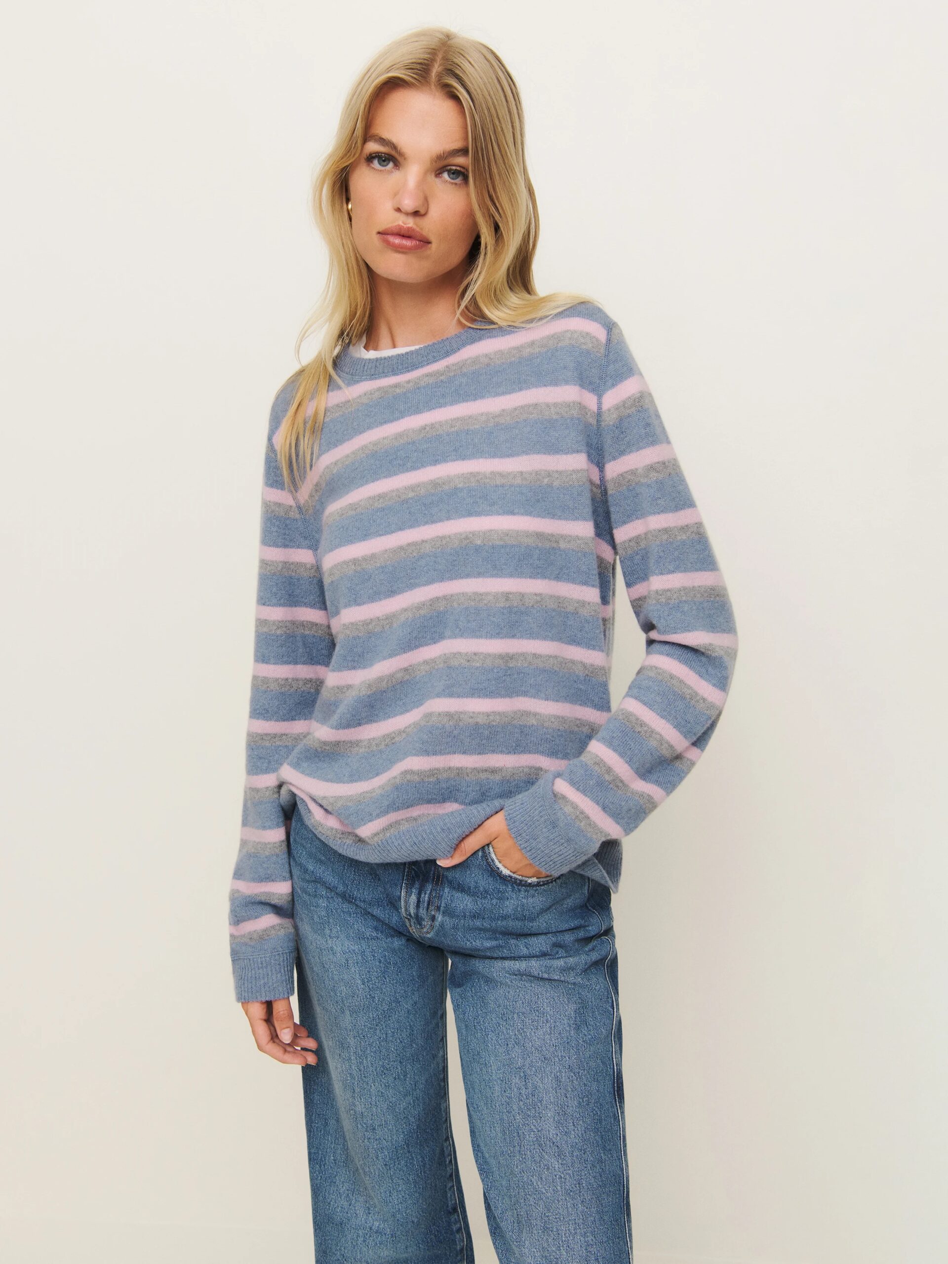 A model wearing a blue, grey, and pink striped cashmere sweater from Reformation. 