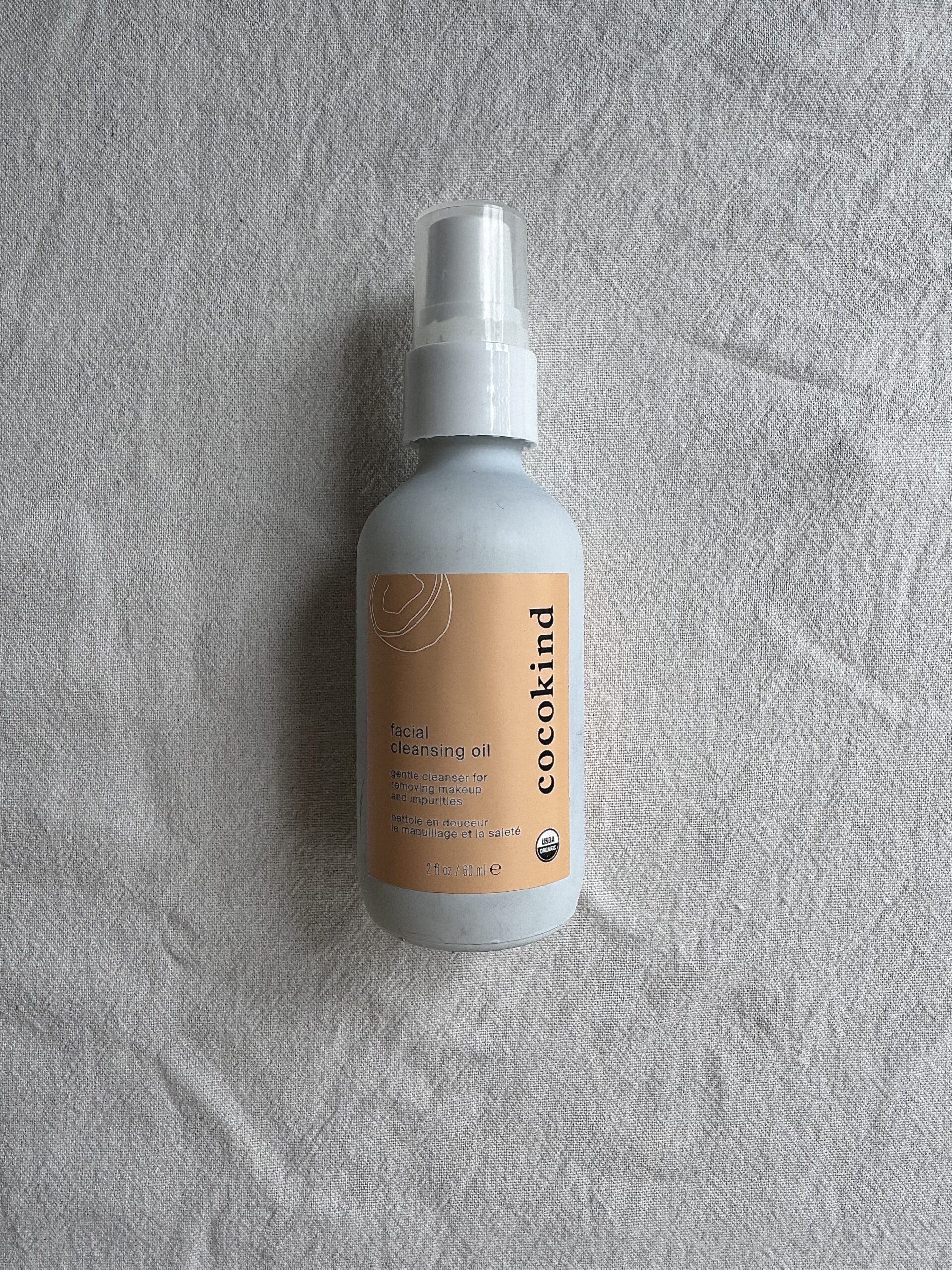 A bottle of cocokind facial cleansing oil on a white fabric surface. 