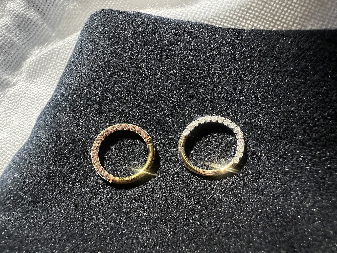 Two gold rings with stones on a black fabric background, illuminated by light.