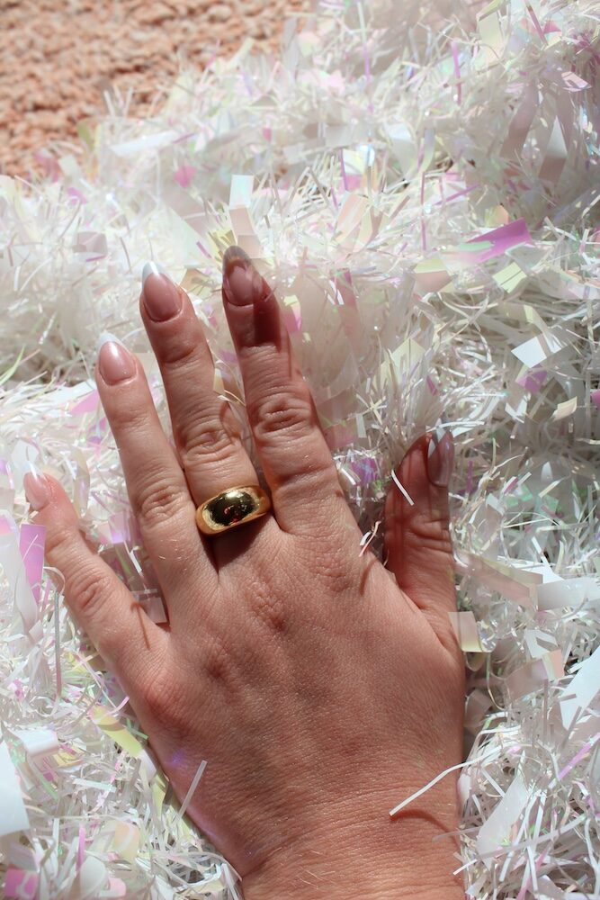 A hand with a gold ring resting on iridescent shredded paper in soft lighting.