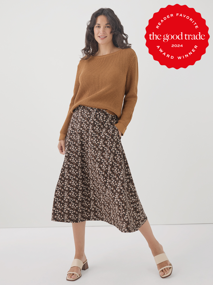 Woman wearing a brown sweater, floral skirt, and sandals stands smiling. A red circular badge in the upper right corner reads "Reader Favorite, The Good Trade, Award Winner, 2024.