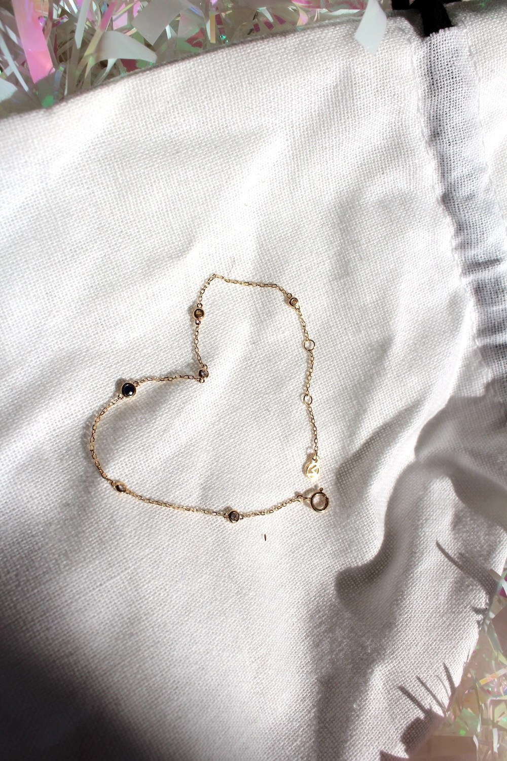 Gold chain arranged in a heart shape on a white fabric surface with a glimmering edge.