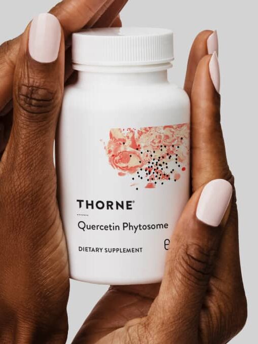 A hand holding a Thorne Quercetin Phytosome dietary supplement bottle. The packaging mentions respiratory support, foundational wellness, allergy relief, and enhanced bioavailability.