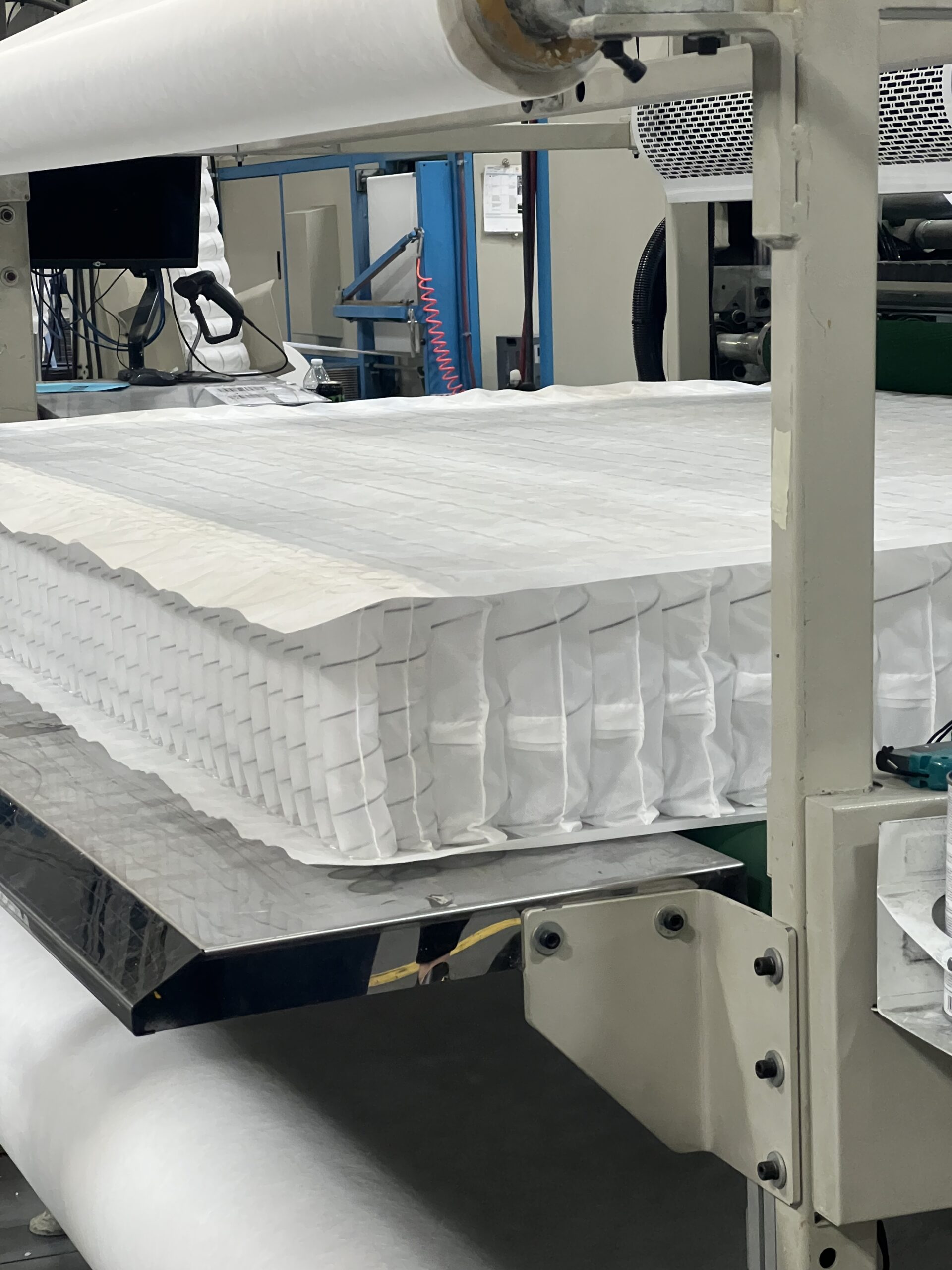 Stack of white mattress springs wrapped in fabric loaded into a production machine in a factory setting.